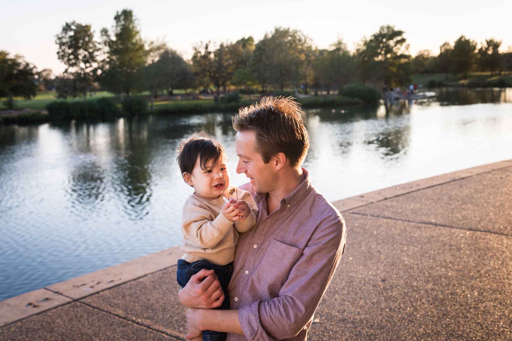 Little boy playing with father wearing pink shirt beside Mueller Lake during a Mueller Lake Park family portrait