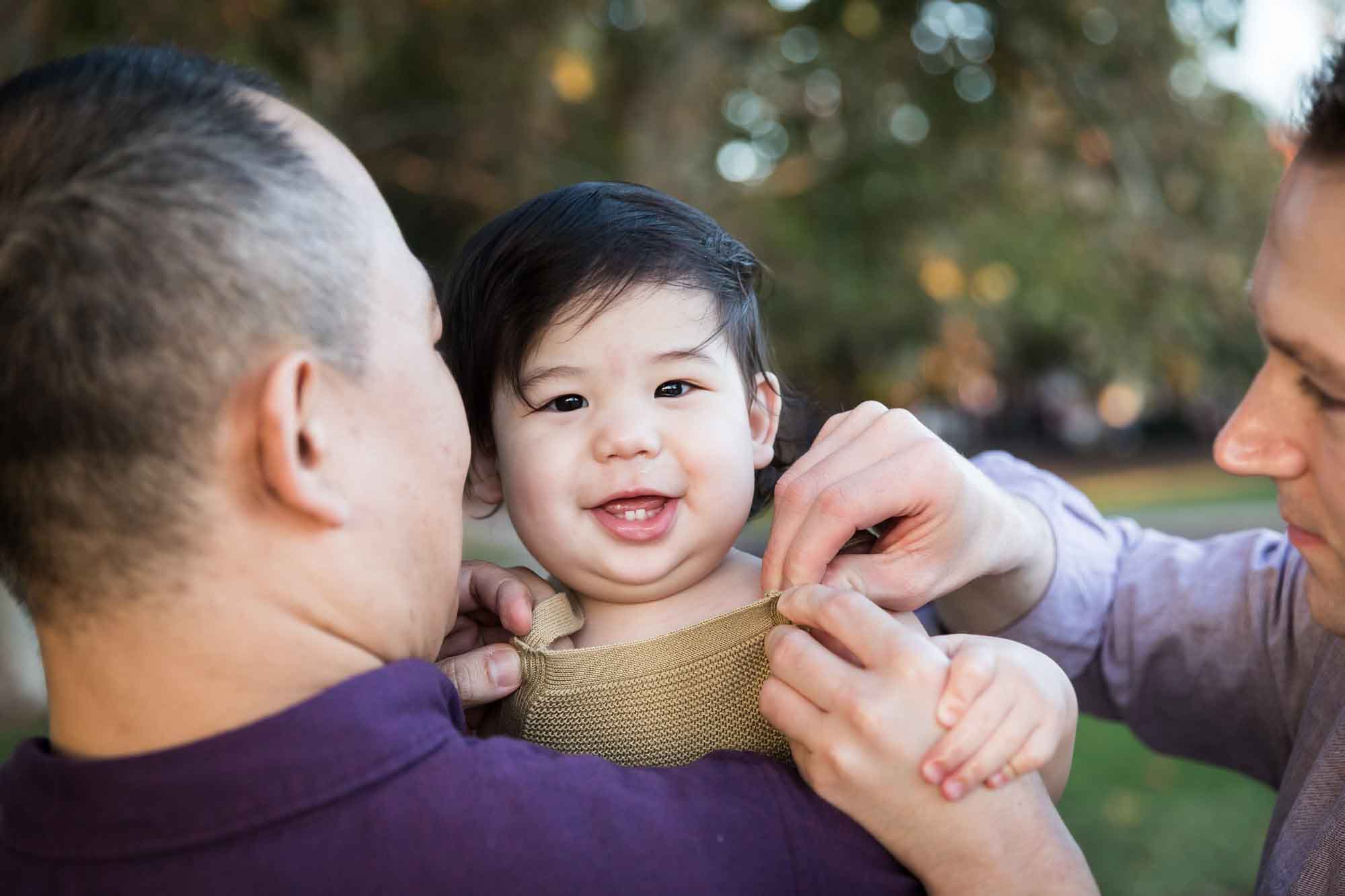Little boy being held over shoulder of father wearing purple shirt while being buttoned up by other father during a Mueller Lake Park family portrait