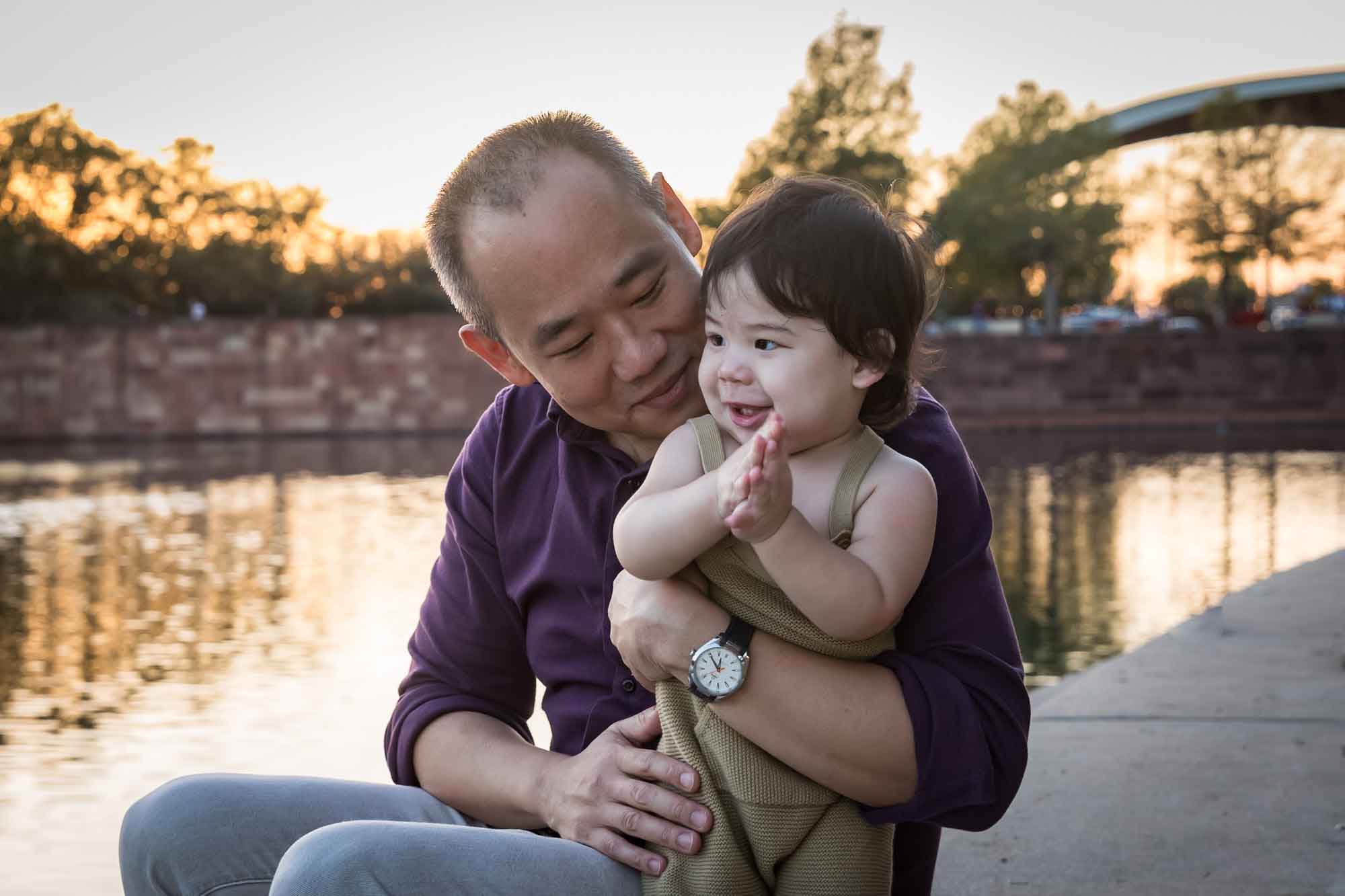 Father and little boy playing on concrete ground beside Mueller Lake during a Mueller Lake Park family portrait