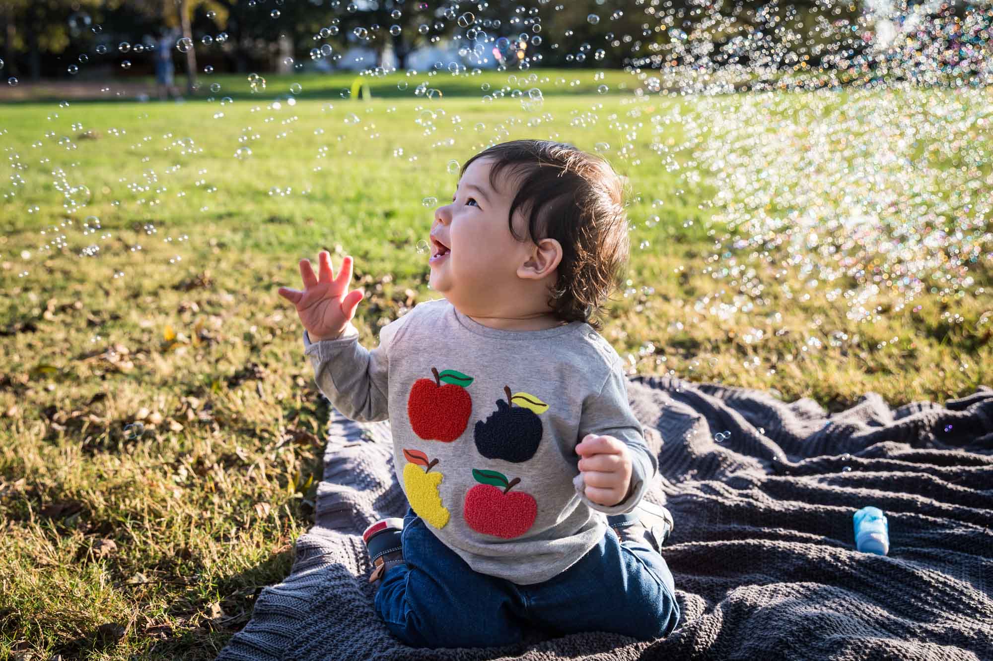 Little boy playing with bubbles while sitting on grass during a Mueller Lake Park family portrait