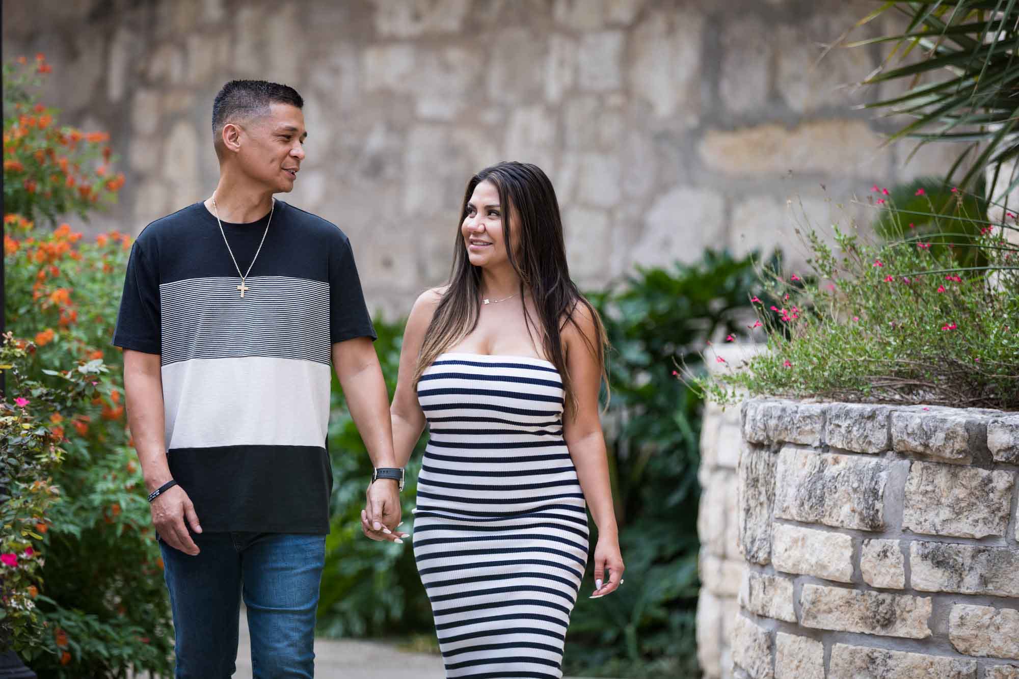 Man wearing striped shirt and jeans holding hands with woman wearing black and white striped, sleeveless dress during a Riverwalk engagement photo shoot
