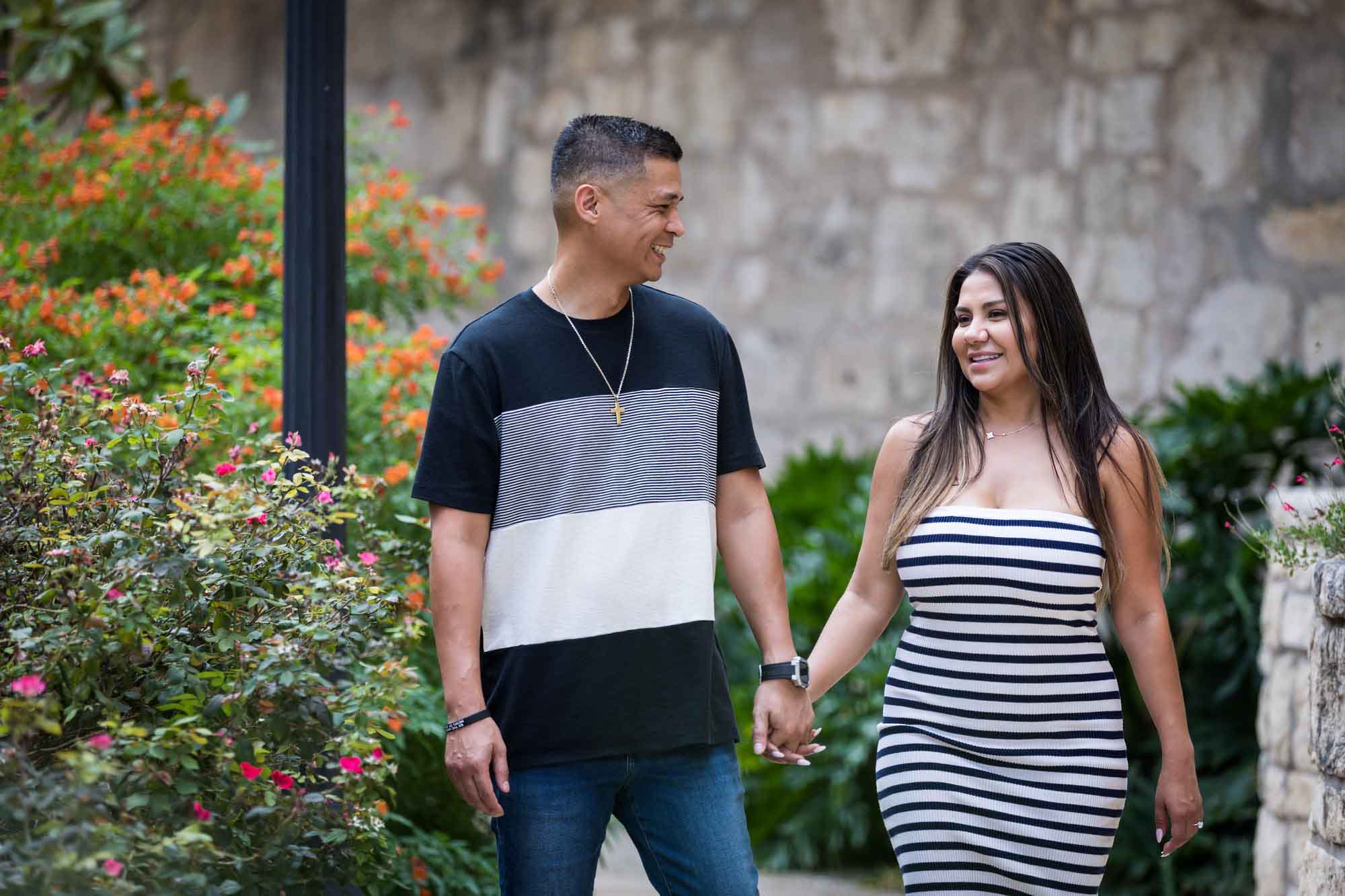 Man wearing striped shirt and jeans holding hands with woman wearing black and white striped, sleeveless dress during a Riverwalk engagement photo shoot