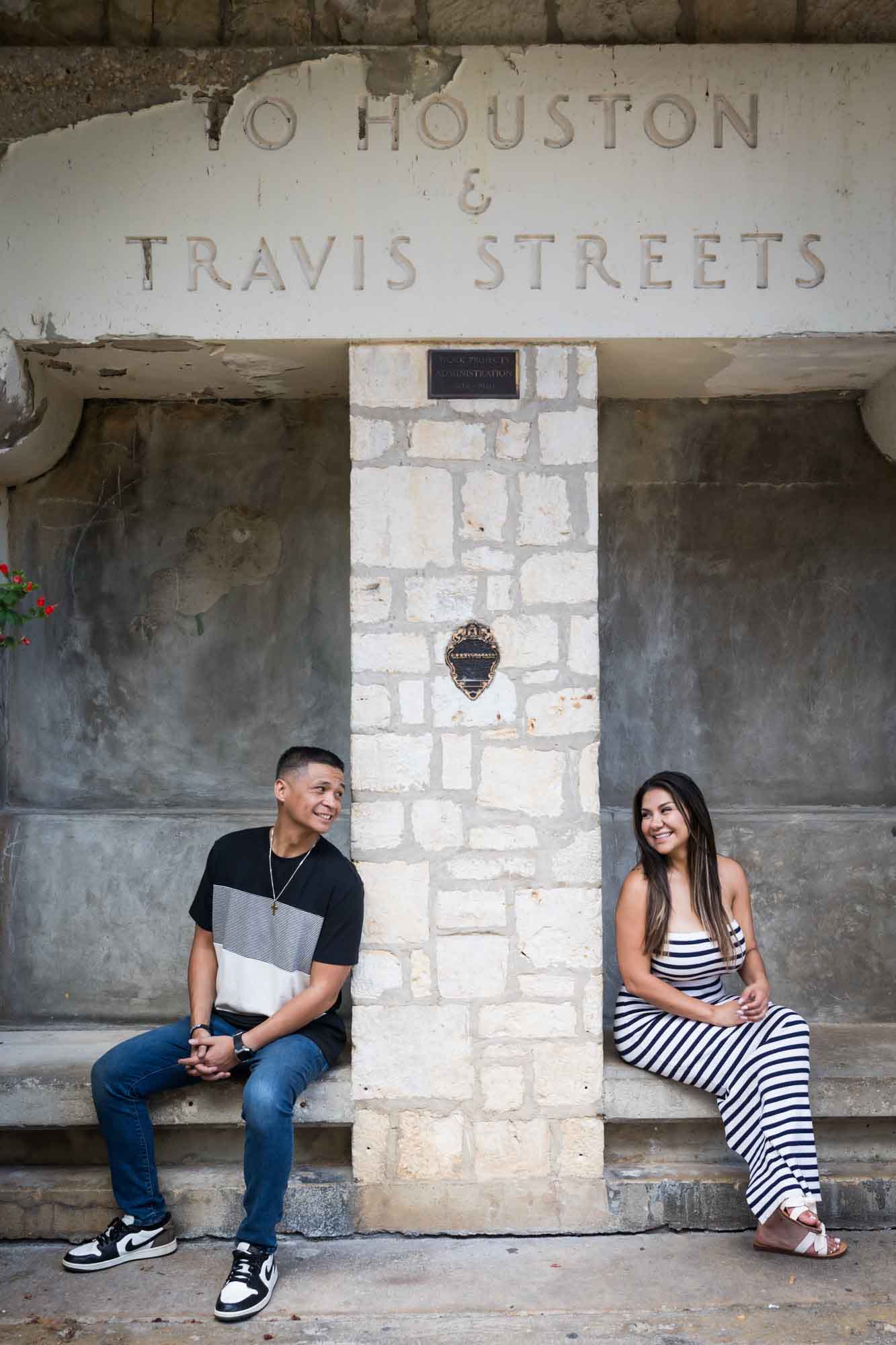 Man and woman looking at each other across from stone pillar while seated on stone benches for an article entitled, ‘When Should I Book My Wedding Photographer?’