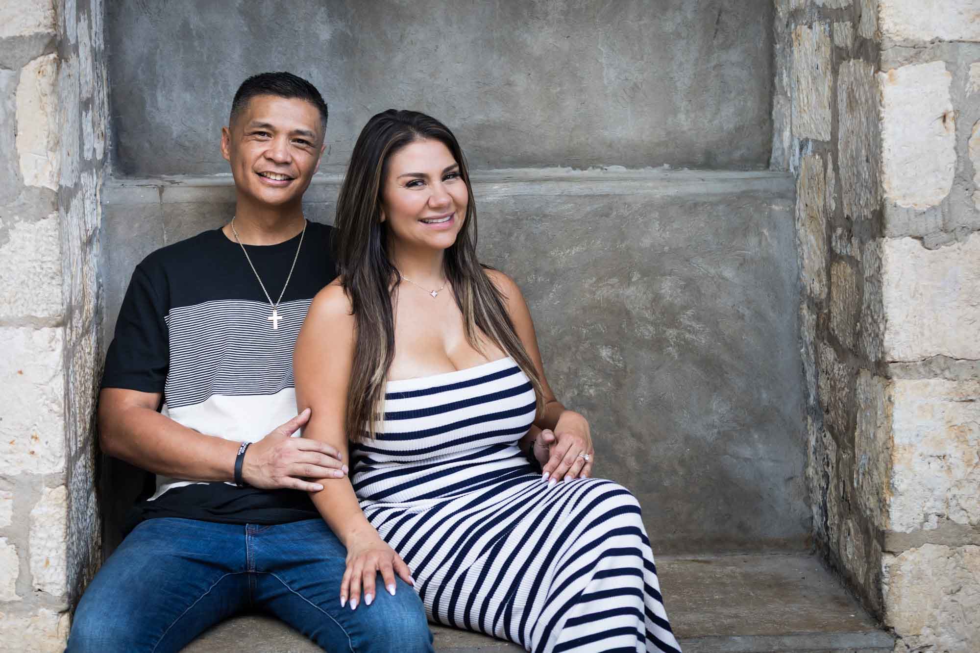 Couple sitting on stone bench with man's hand on woman's arm for an article entitled, ‘When Should I Book My Wedding Photographer?’