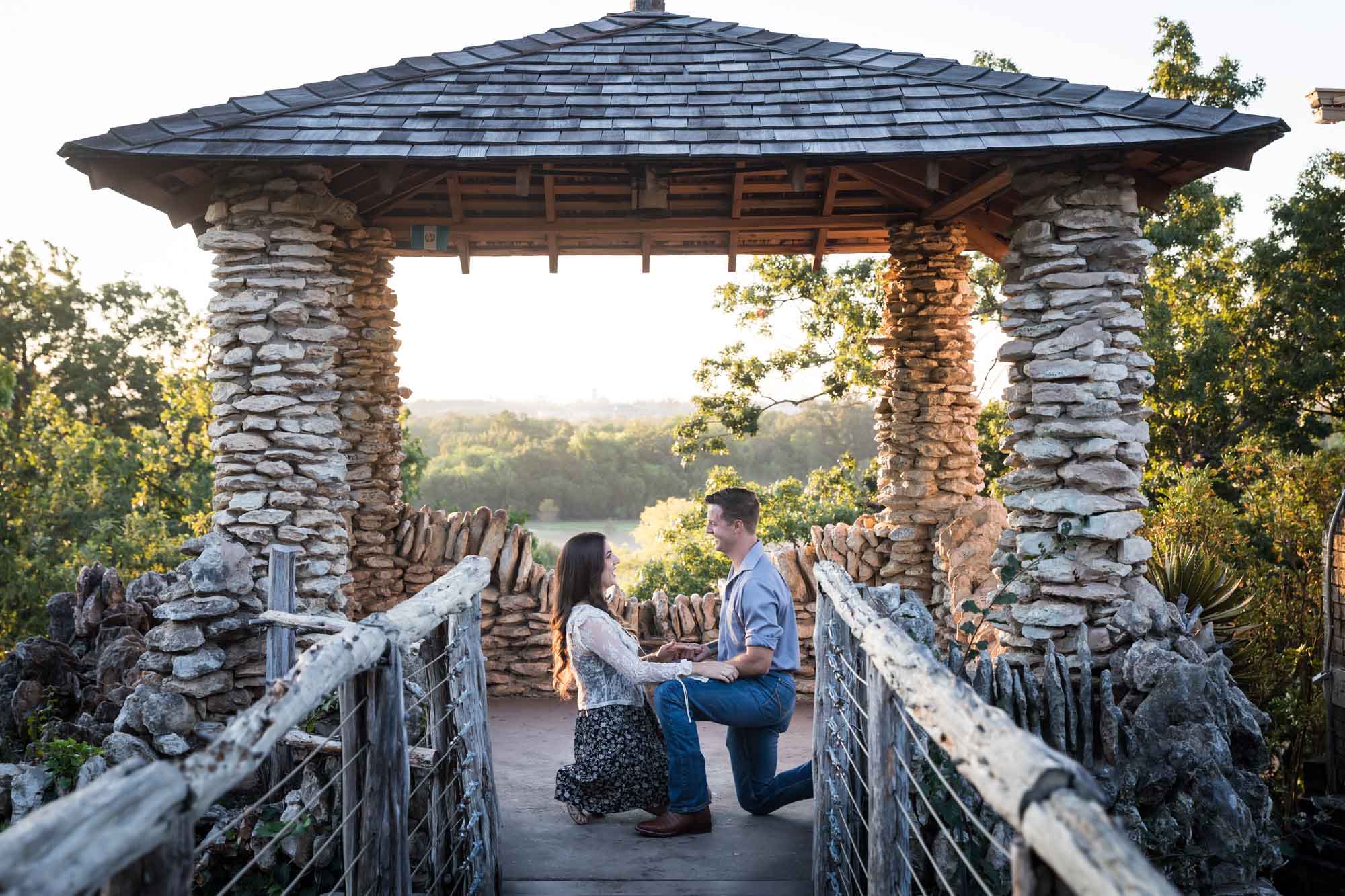 Man proposing on one knee to woman in middle of stone building during Japanese Tea Garden surprise proposal by Kelly Williams San Antonio wedding photographer