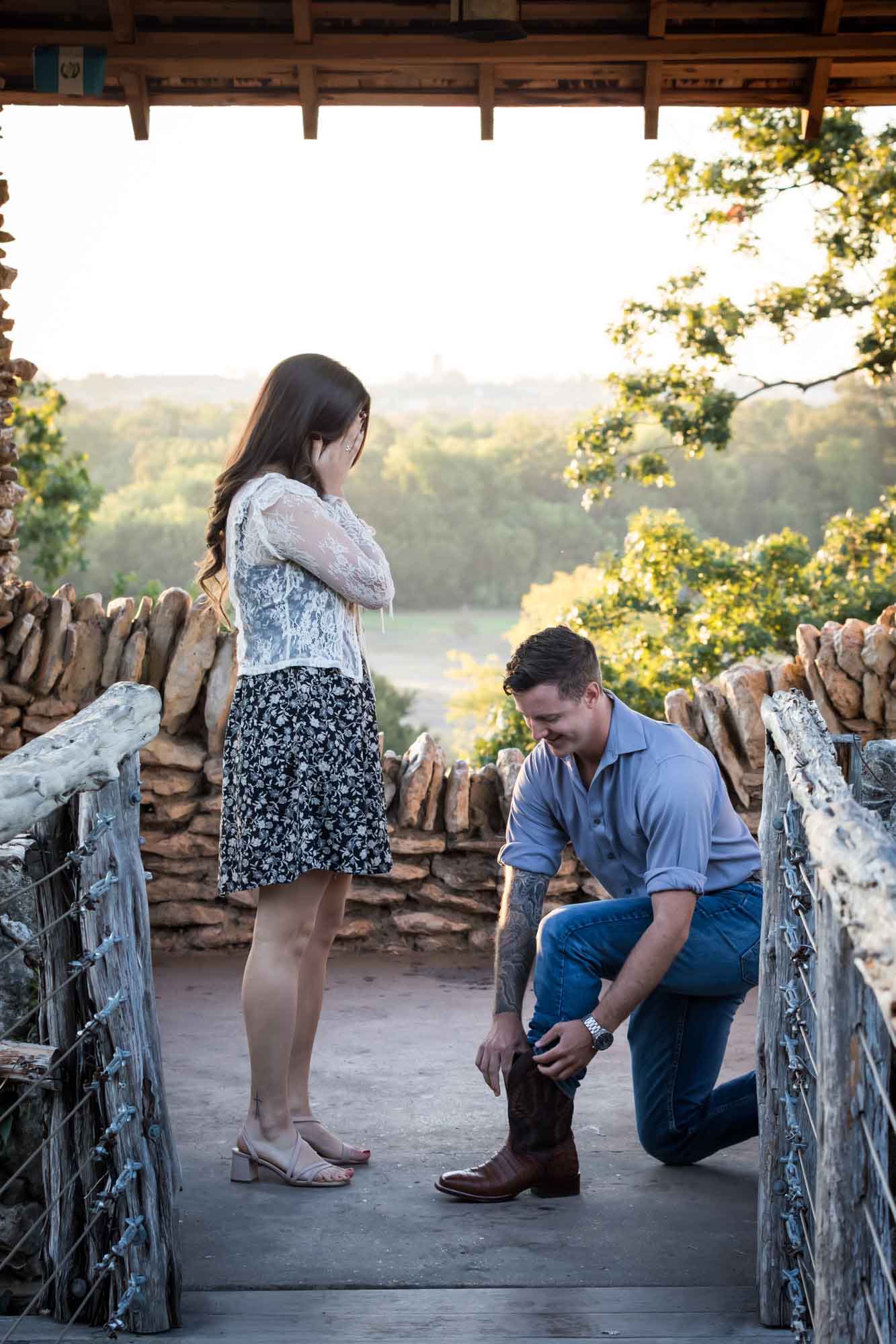 Man getting ring out of boot while proposing to woman in middle of stone building during Japanese Tea Garden surprise proposal by Kelly Williams San Antonio wedding photographer