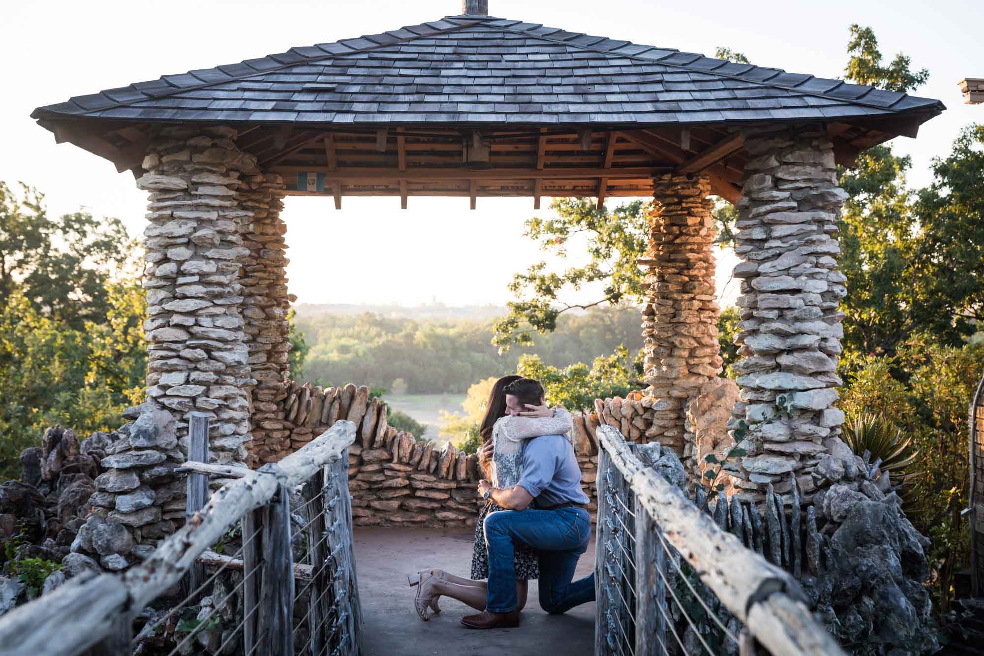 Man proposing on one knee to woman in middle of stone building during Japanese Tea Garden surprise proposal by Kelly Williams San Antonio wedding photographer