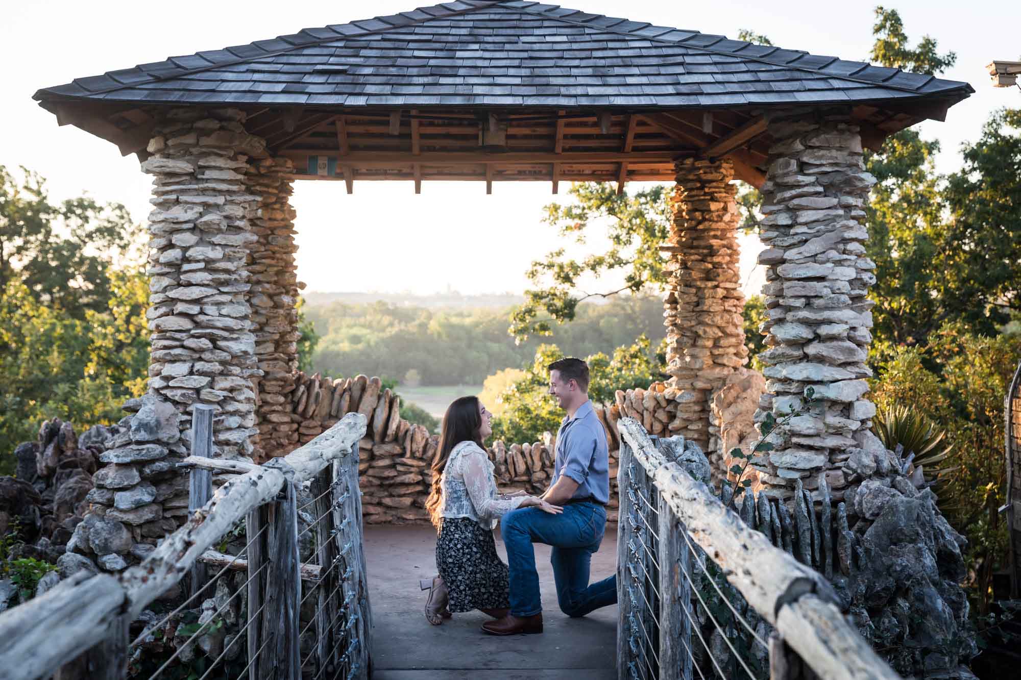 Man proposing on one knee to woman in middle of stone building during Japanese Tea Garden surprise proposal by Kelly Williams San Antonio wedding photographer