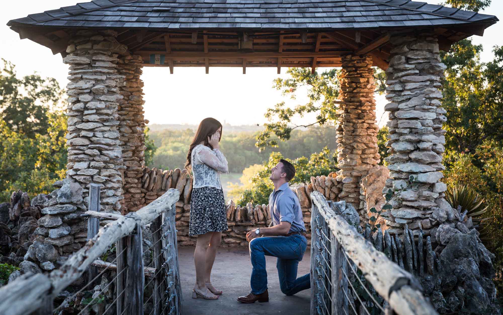 Man proposing on one knee to woman in middle of stone building during Japanese Tea Garden surprise proposal by Kelly Williams San Antonio wedding photographer
