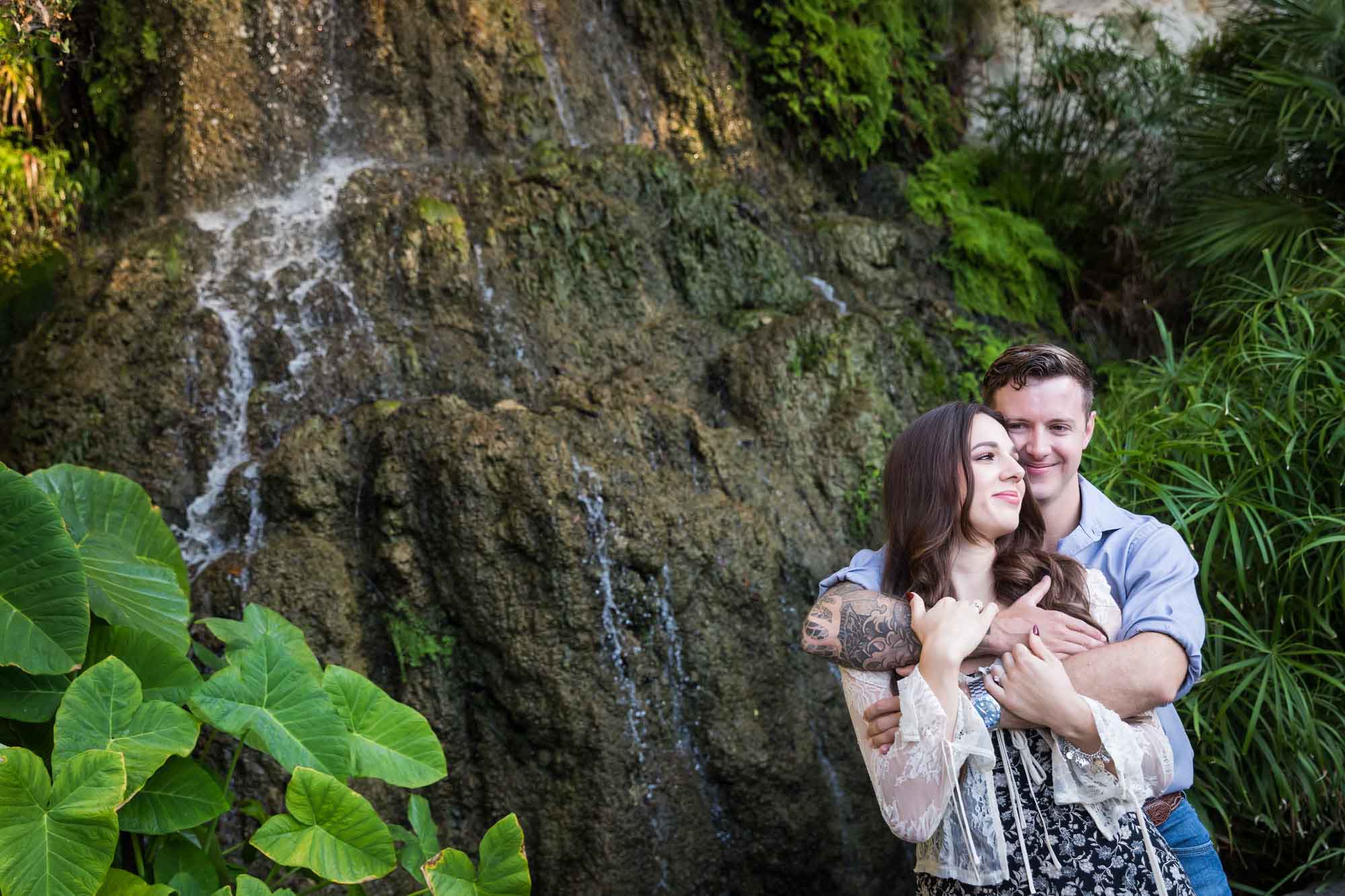 Couple hugging in front of moss-covered waterfall during a Japanese Tea Garden engagement portrait 