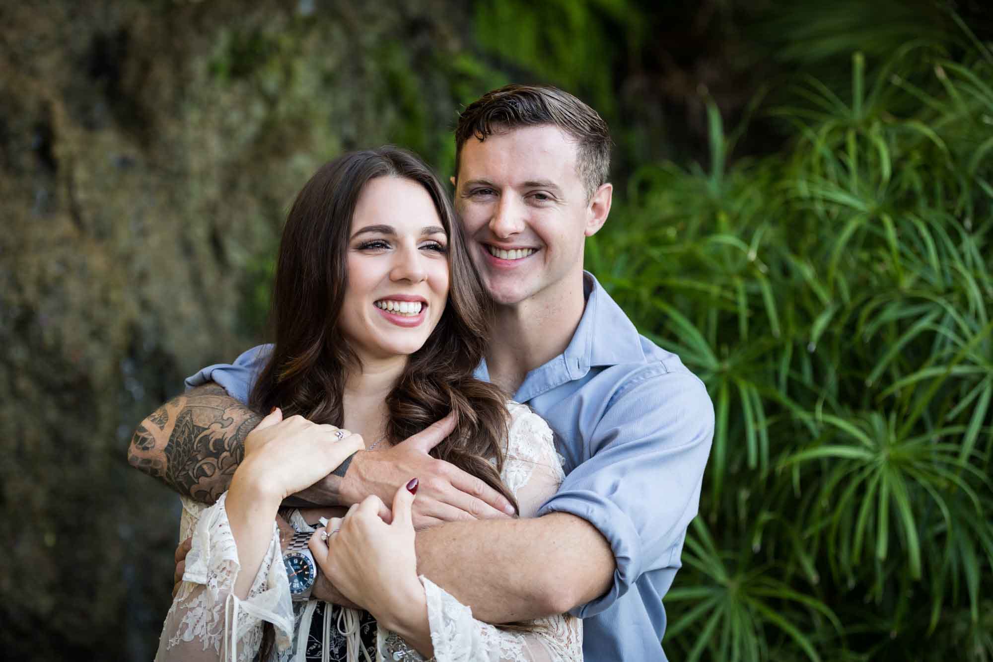 Couple hugging in front of moss-covered waterfall during a Japanese Tea Garden engagement portrait 
