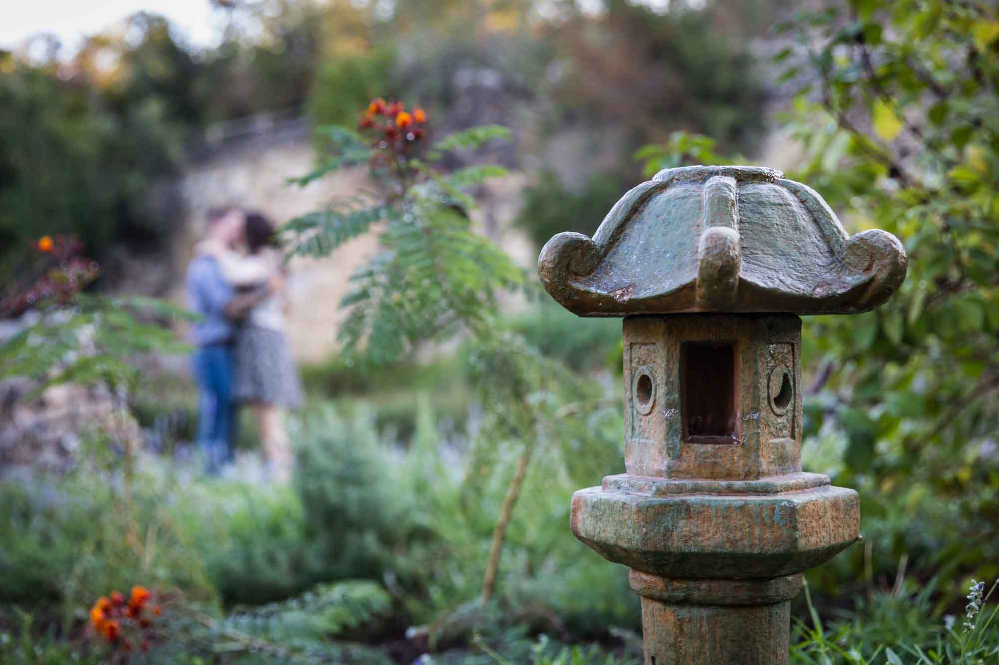 Couple out of focus behind Chinese stone lantern during a Japanese Tea Garden engagement portrait 