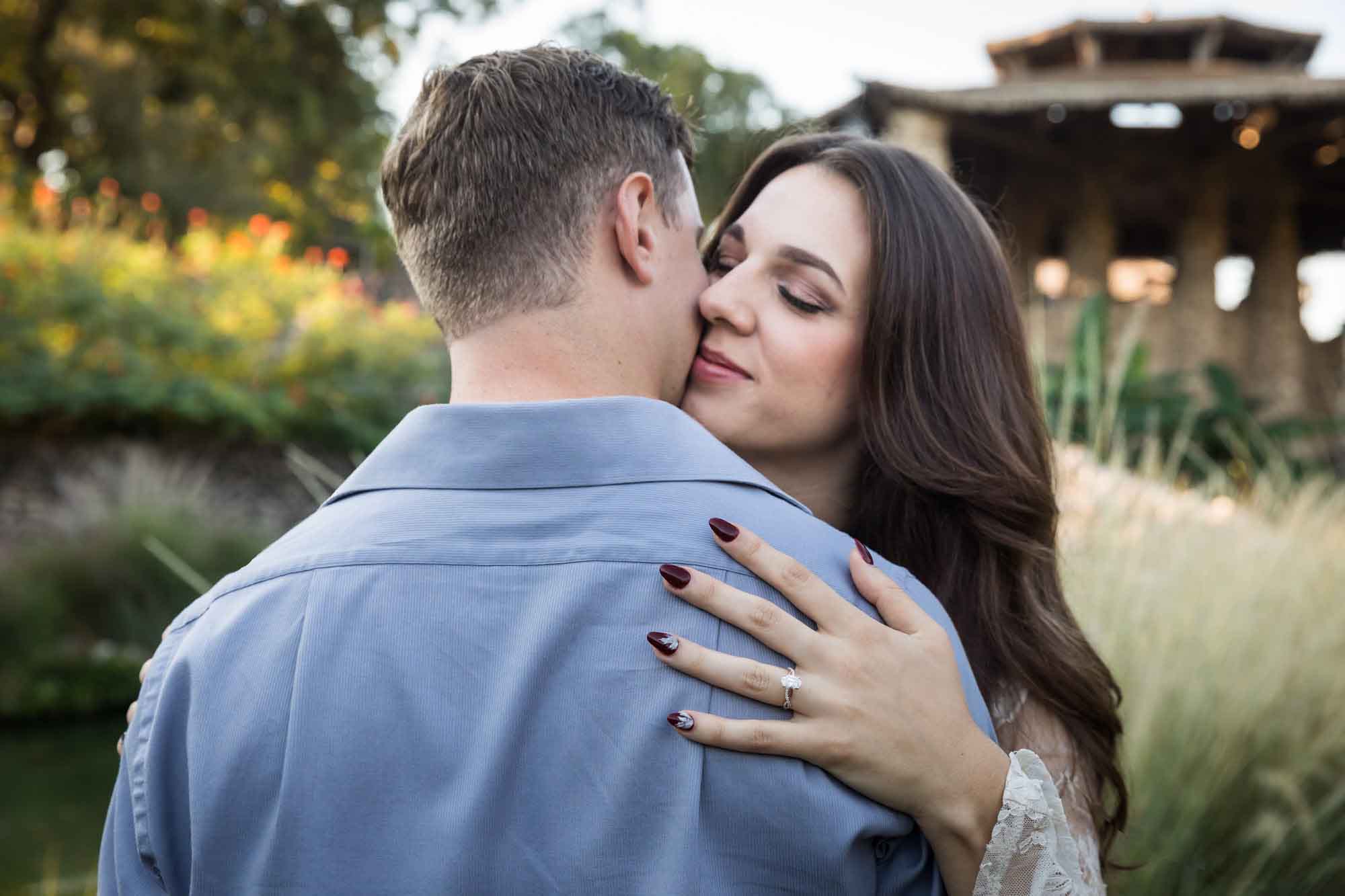 Close up of a man kissing a woman with her hand on the man's back showing her engagement ring for an article on ‘Where do I Start with Wedding Planning?’