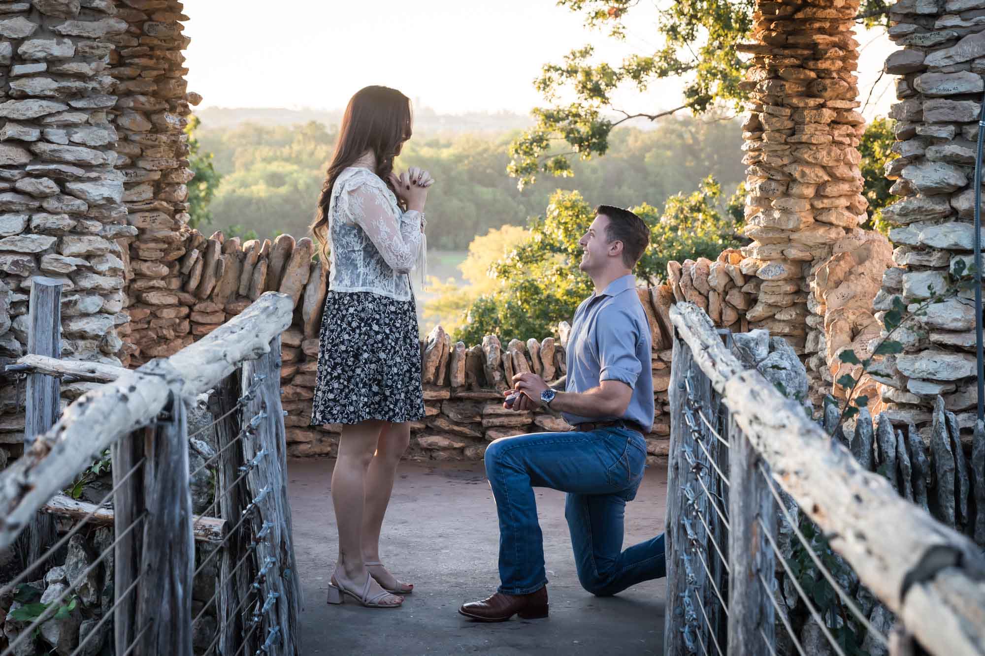 Man proposing on one knee to woman in middle of stone building during Japanese Tea Garden surprise proposal by Kelly Williams San Antonio wedding photographer