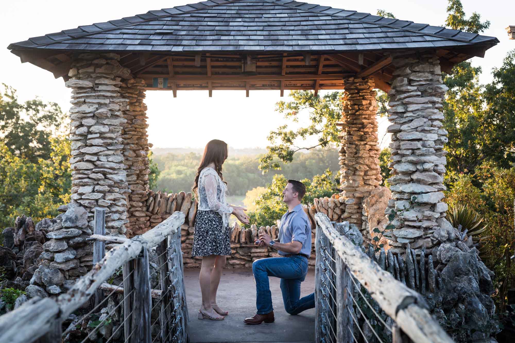 Man proposing on one knee to woman in middle of stone building during Japanese Tea Garden surprise proposal by Kelly Williams San Antonio wedding photographer