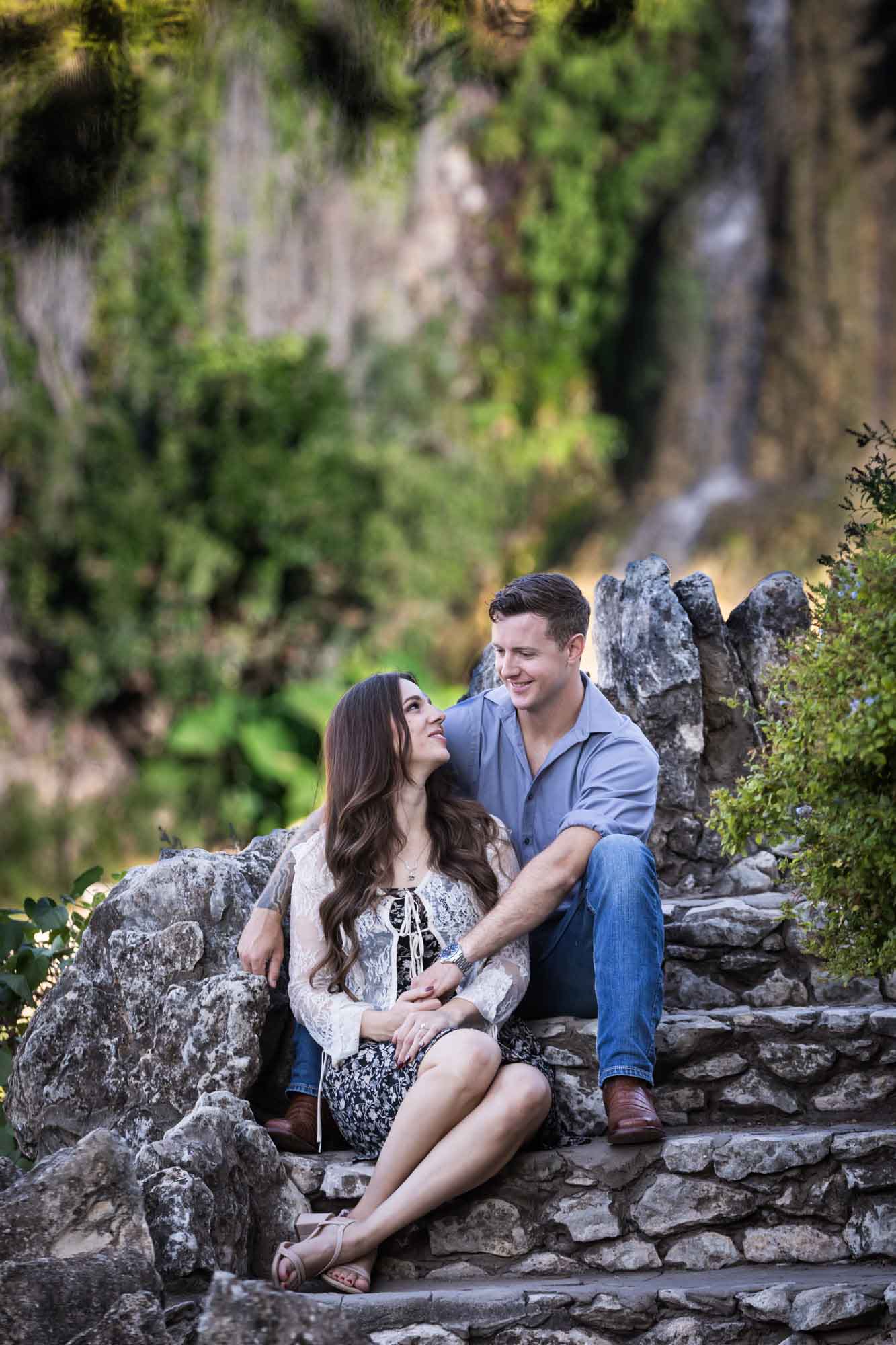 Couple sitting on stone steps in front of waterfall during a Japanese Tea Garden engagement portrait 