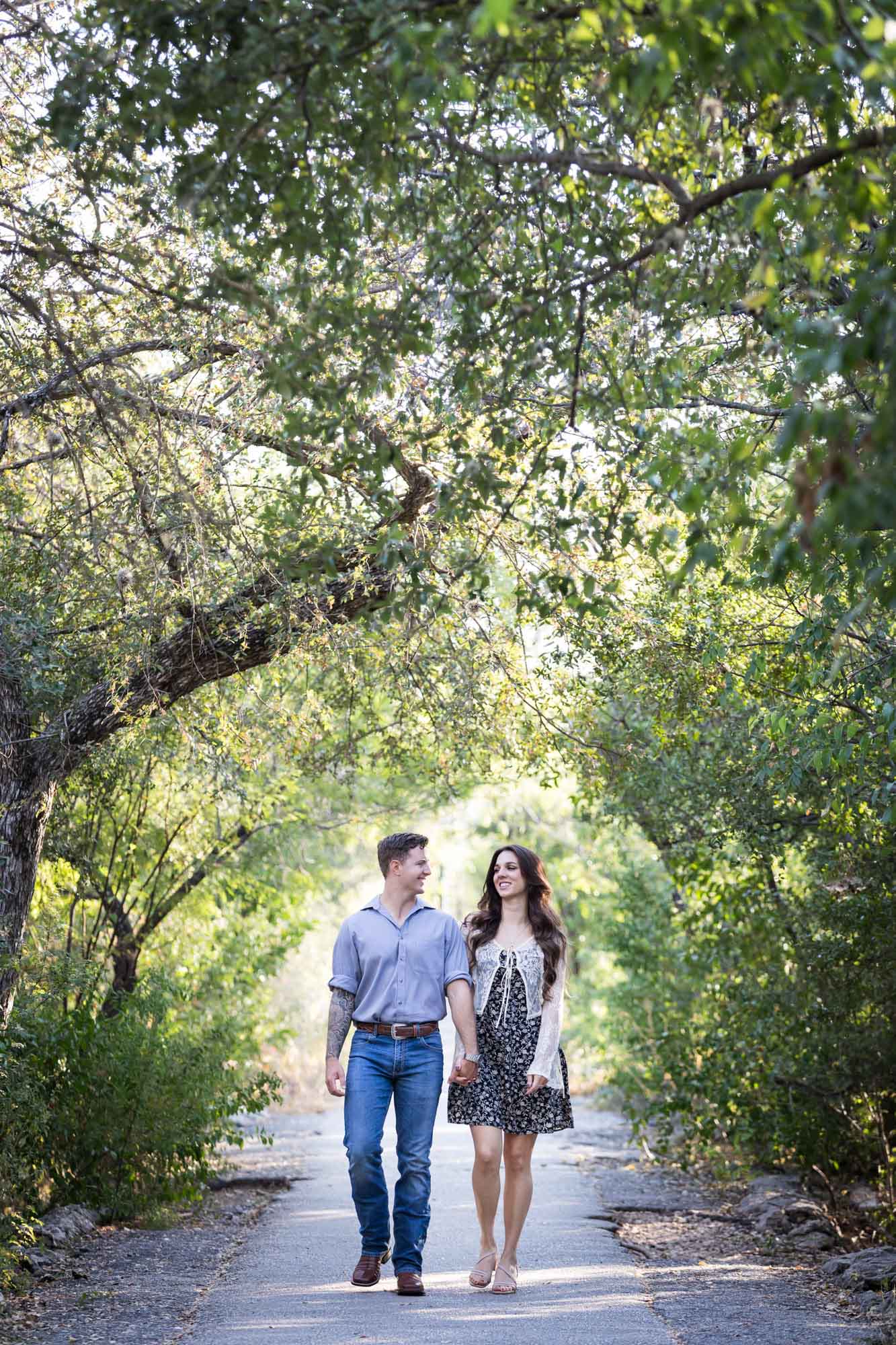 Couple walking under tree branches in Brackenridge Park during a Japanese Tea Garden engagement portrait 