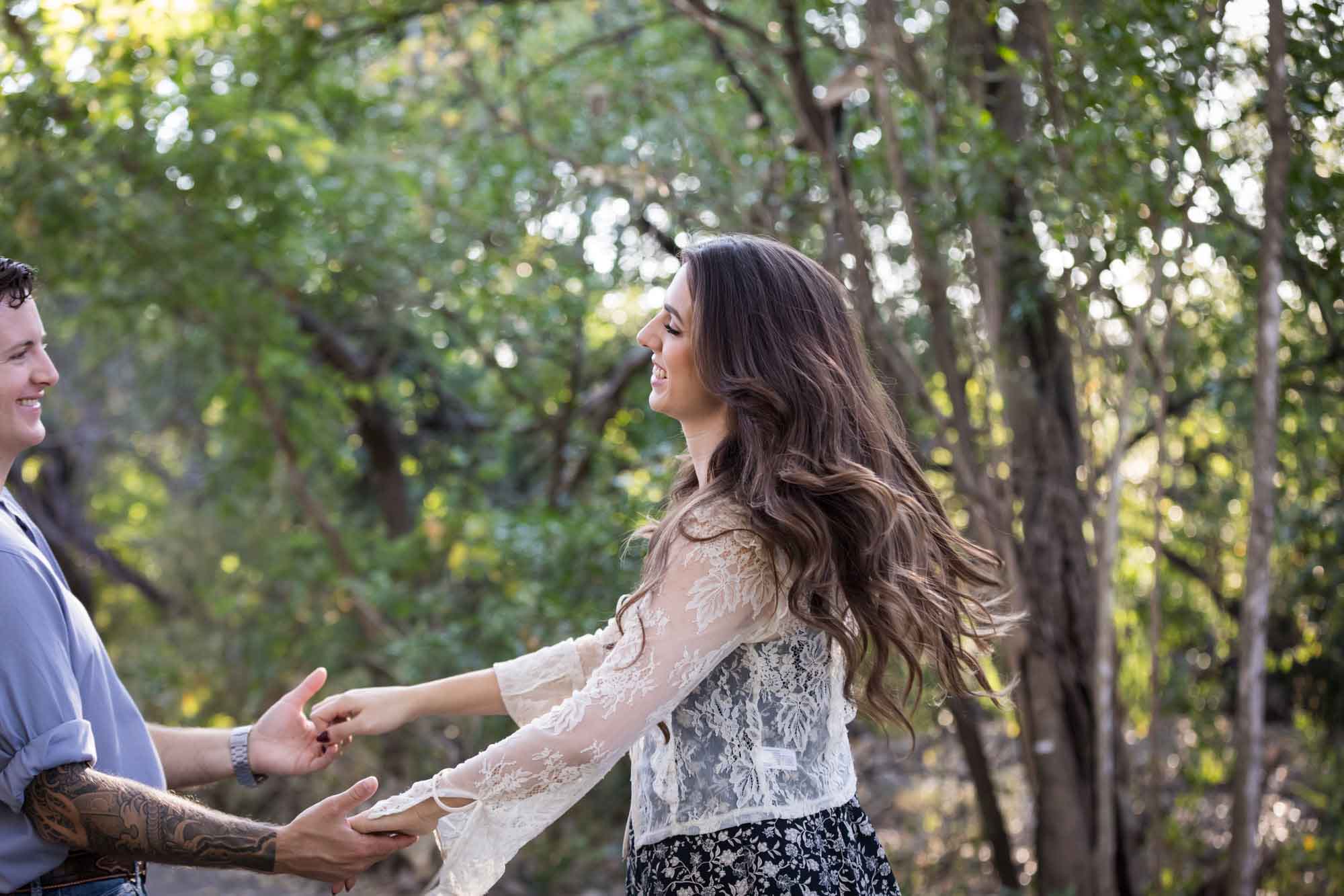 Couple dancing under tree branches in Brackenridge Park during a Japanese Tea Garden engagement portrait by San Antonio wedding photographer Kelly Williams