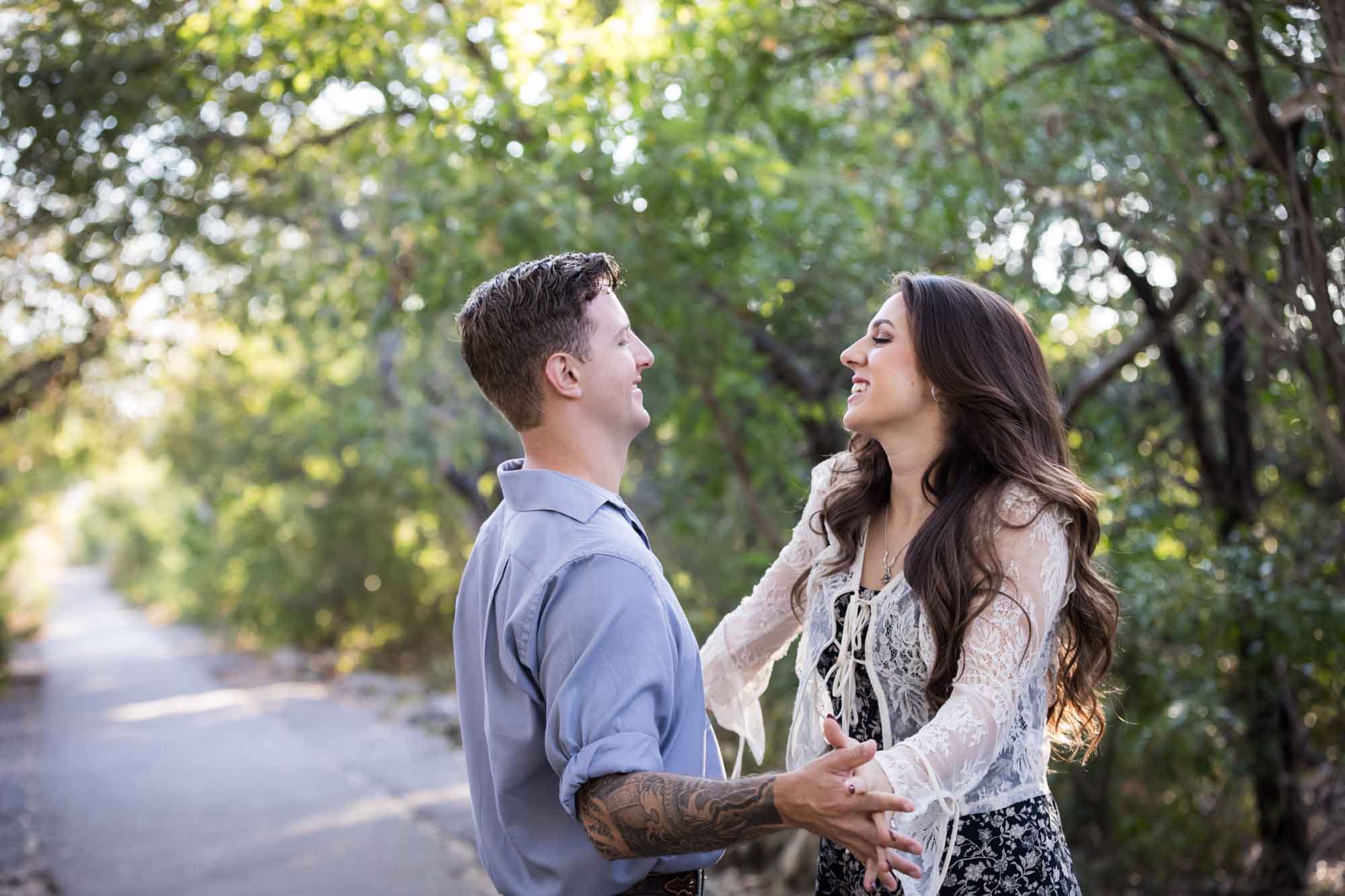 Couple dancing under tree branches in Brackenridge Park during a Japanese Tea Garden engagement portrait by San Antonio wedding photographer Kelly Williams