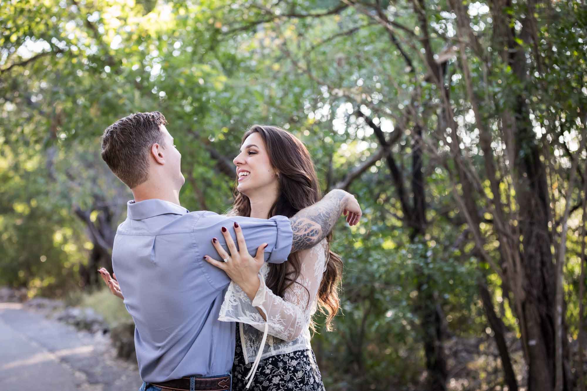 Couple dancing under tree branches in Brackenridge Park during a Japanese Tea Garden engagement portrait by San Antonio wedding photographer Kelly Williams