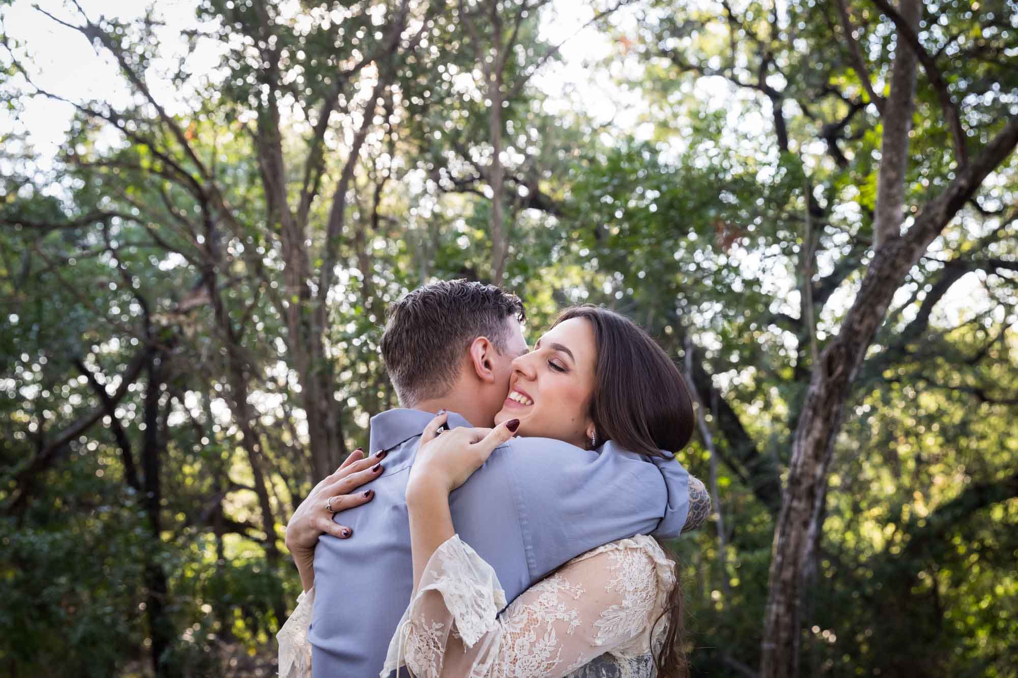 Couple hugging under tree branches in Brackenridge Park during a Japanese Tea Garden engagement portrait by San Antonio wedding photographer Kelly Williams