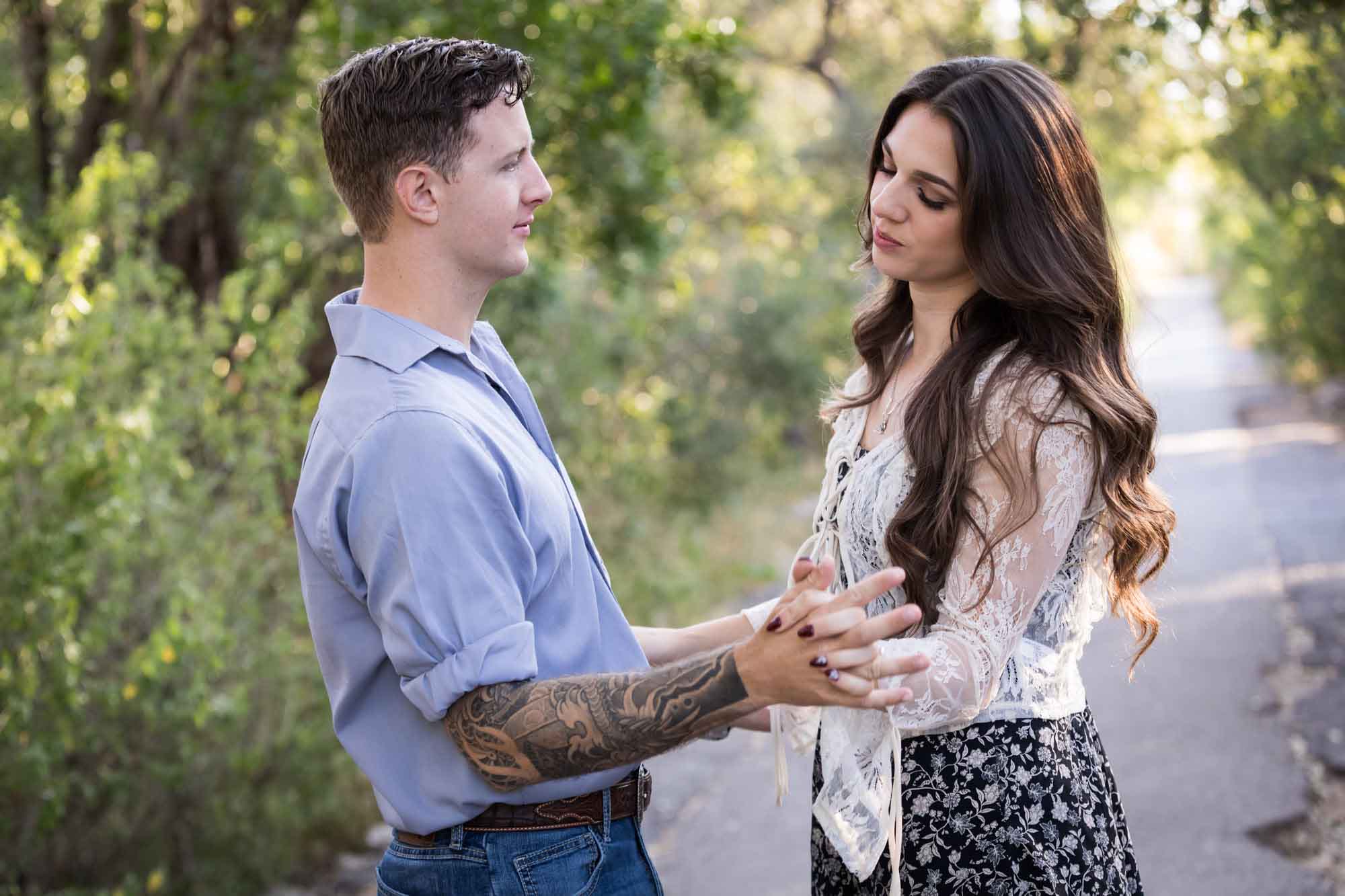 Woman showing engagement ring to man under tree branches in Brackenridge Park during a Japanese Tea Garden engagement portrait by San Antonio wedding photographer Kelly Williams