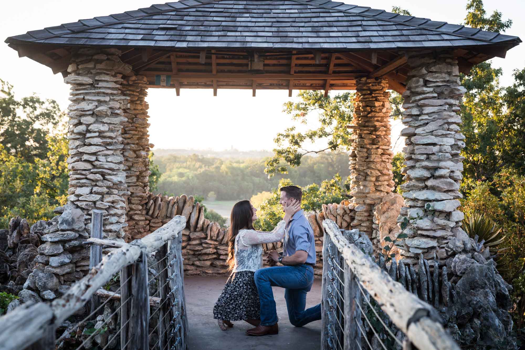 Man proposing on one knee to woman in middle of stone building during Japanese Tea Garden surprise proposal by Kelly Williams San Antonio wedding photographer