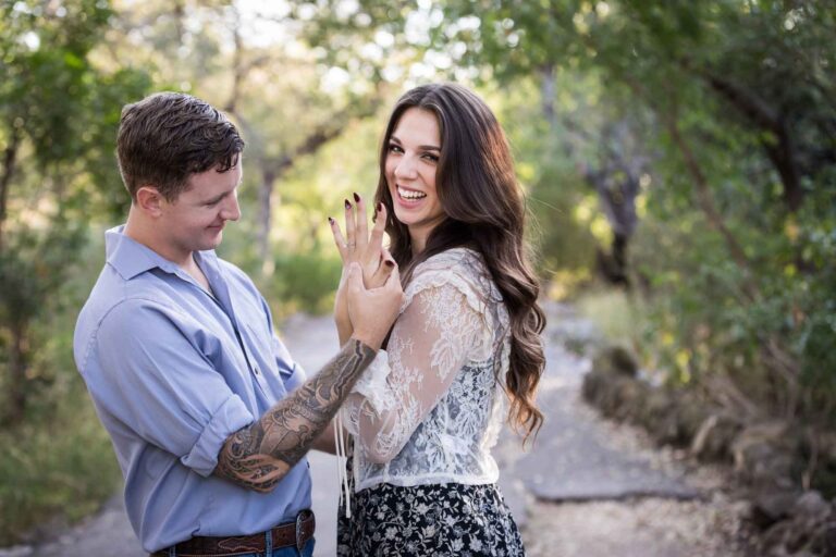 Couple looking at engagement ring under tree branches in Brackenridge Park during a Japanese Tea Garden engagement portrait by San Antonio wedding photographer Kelly Williams
