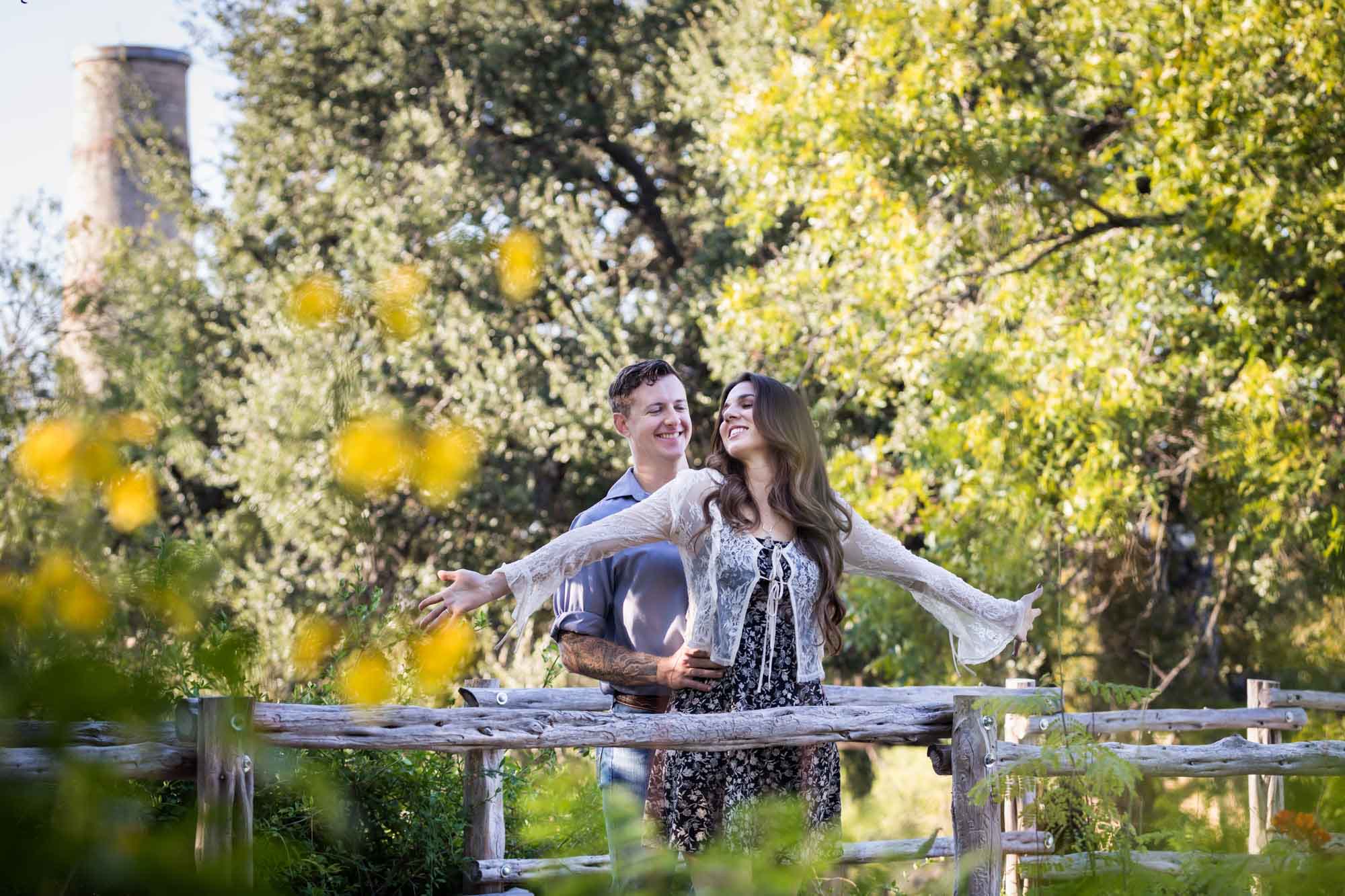 Couple hugging in front of wooden railing with woman's arms outstretched for an article on ‘Where do I Start with Wedding Planning?’