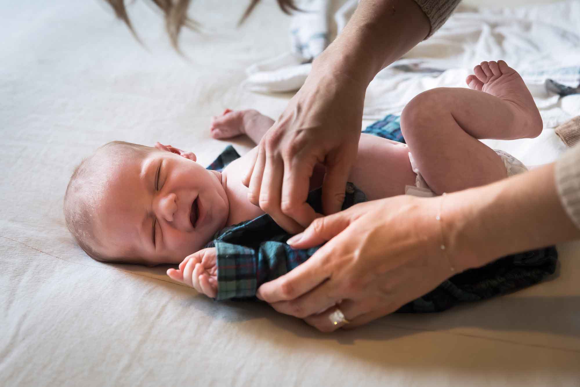 Mother's hands changing crying baby out of shirt while laying on bed during an Austin newborn portrait session