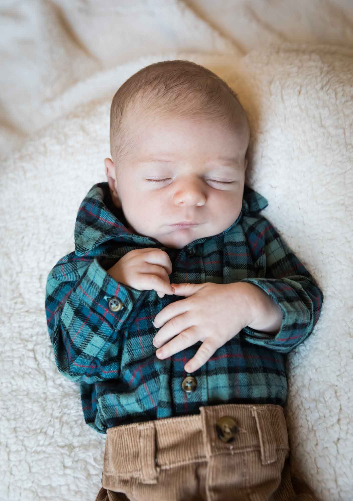 Baby boy wearing green and blue plaid shirt and brown corduroy pants resting on white, fleece blanket during an Austin newborn portrait session