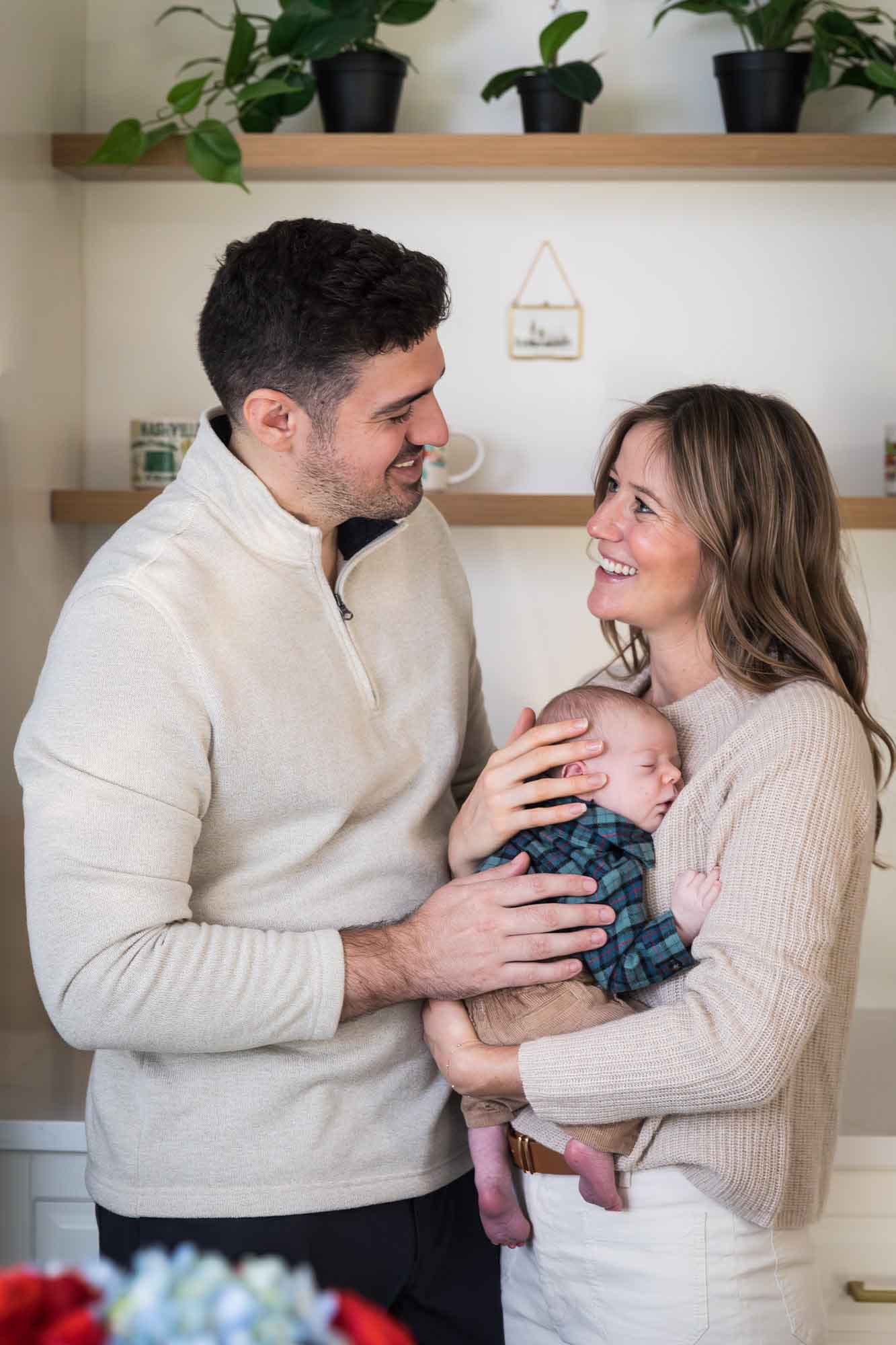 Mother and father holding baby boy wearing plaid shirt standing in white kitchen during an Austin newborn portrait session