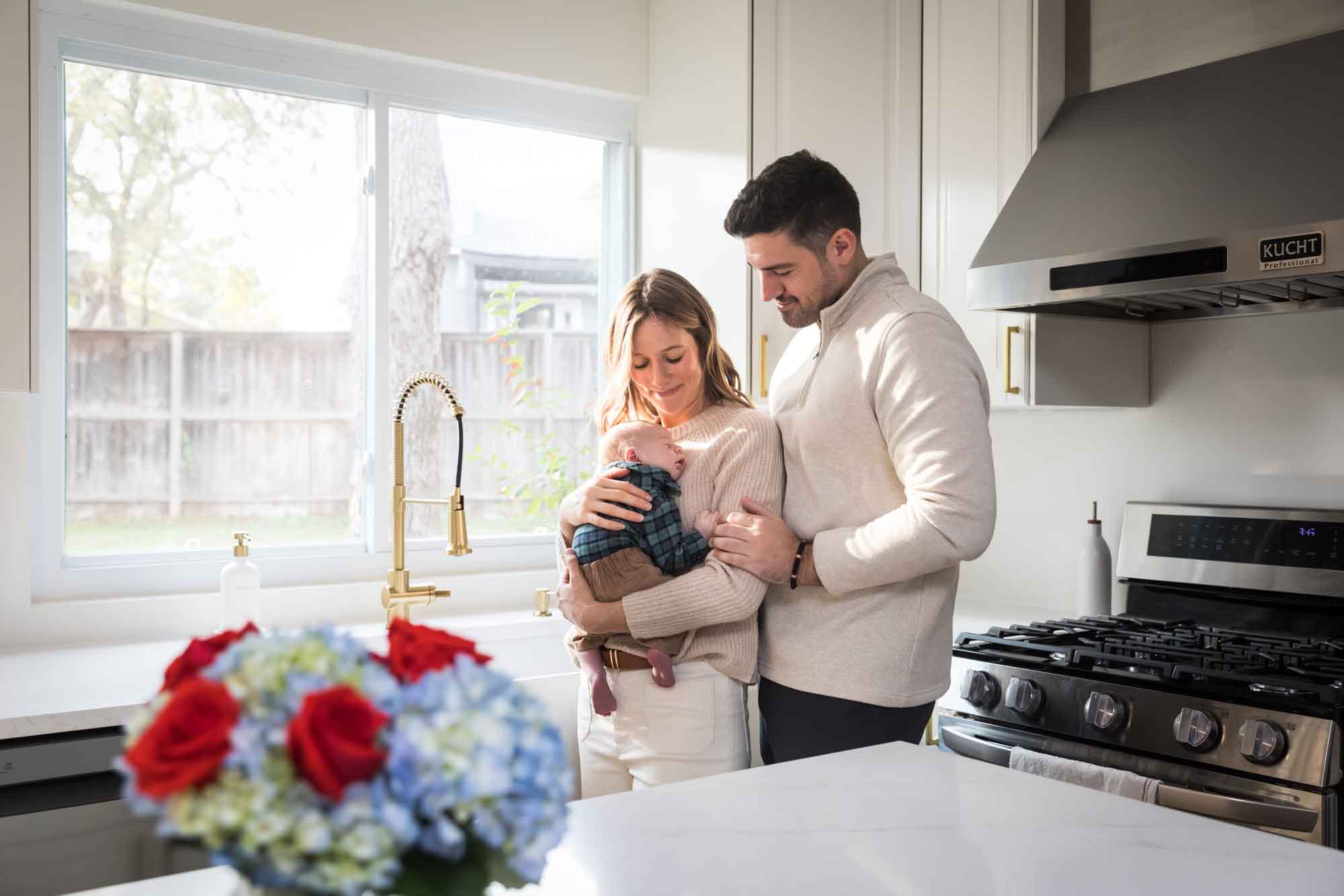 Mother and father holding baby boy wearing plaid shirt standing in white kitchen during an Austin newborn portrait session