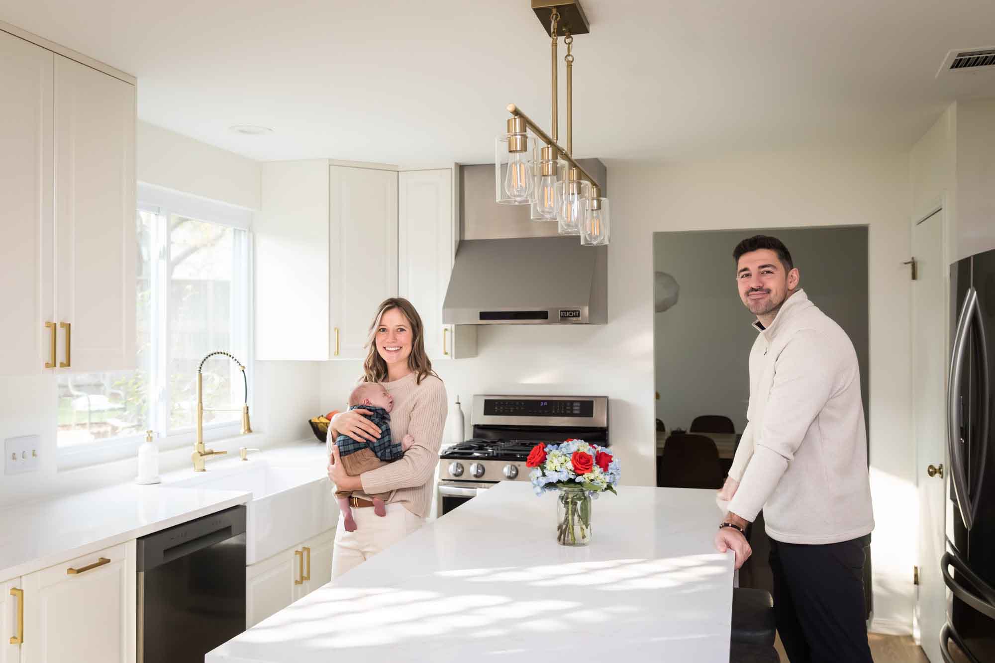 Mother holding baby boy wearing plaid shirt and father standing in white kitchen during an Austin newborn portrait session