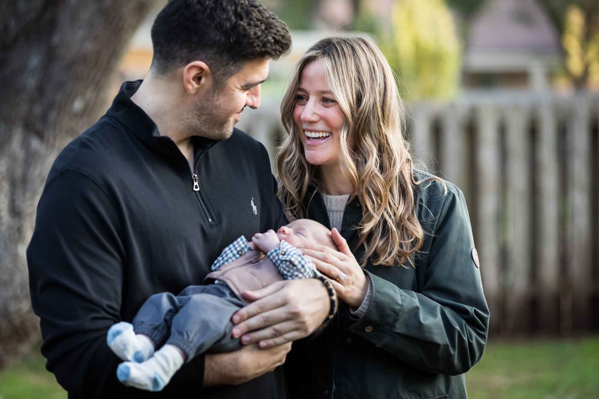 Mother and father looking at each other while holding newborn baby boy in backyard during an Austin newborn portrait session