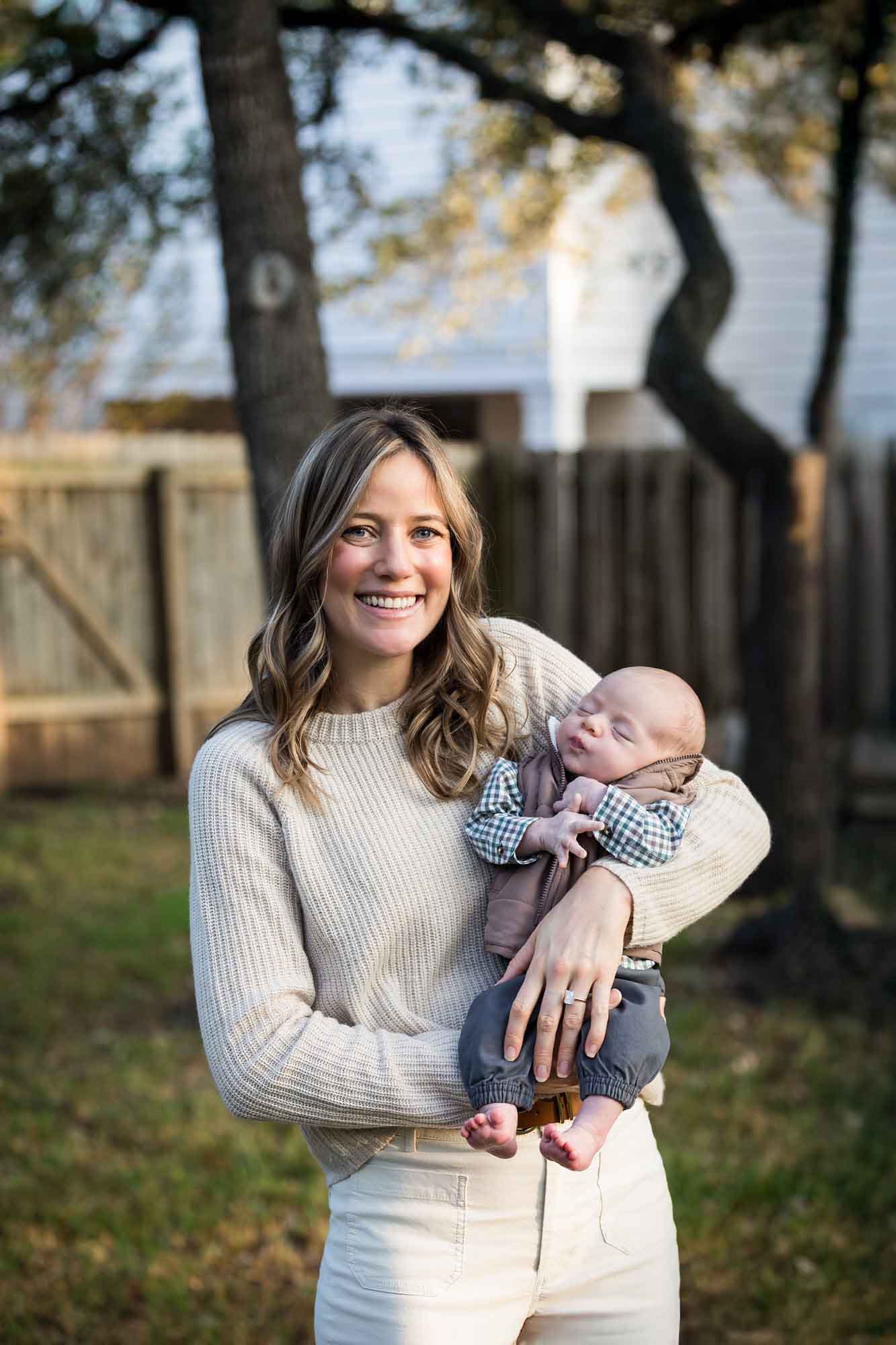 Mother holding newborn baby boy in backyard during an Austin newborn portrait session