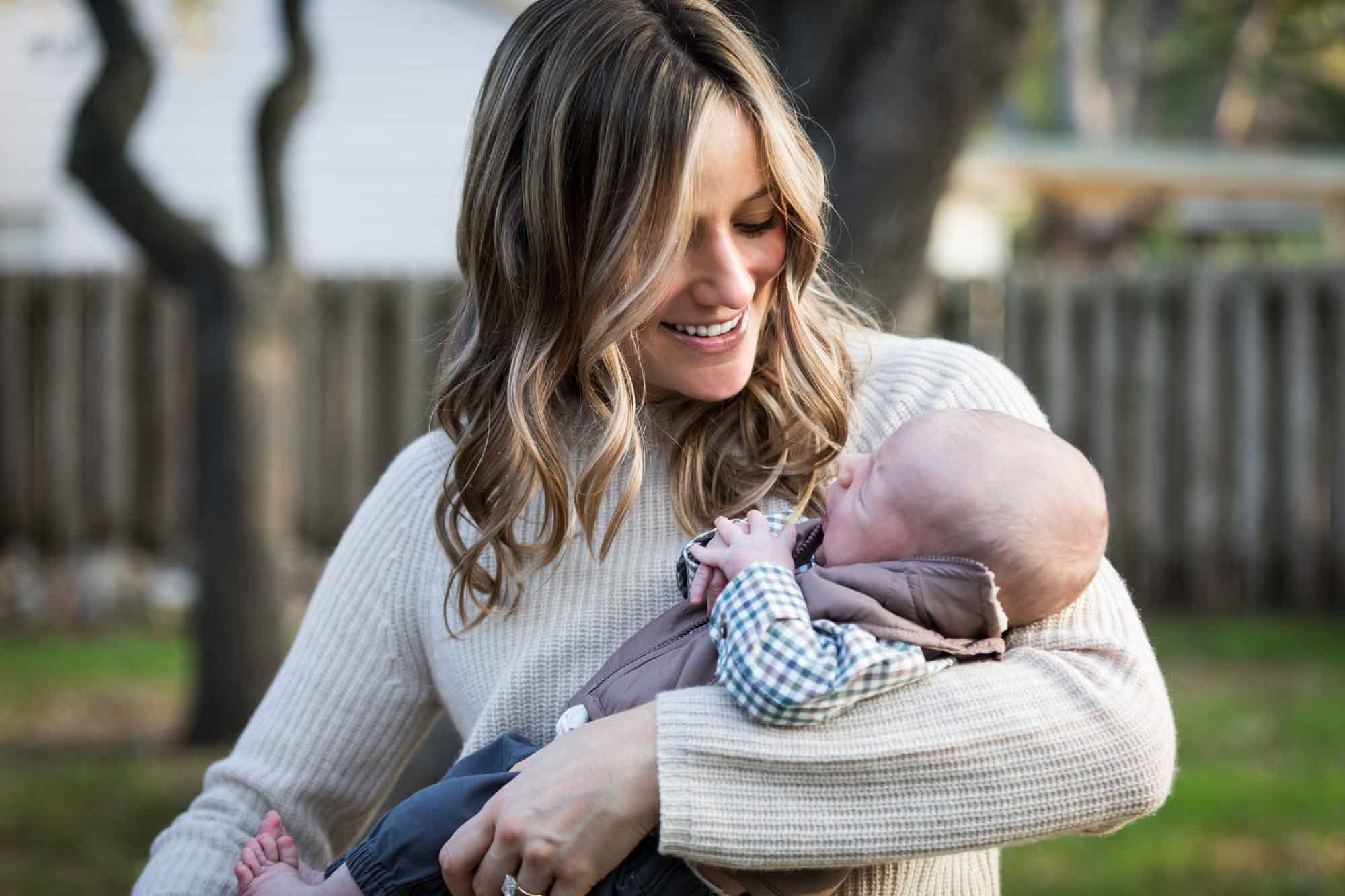 Mother smiling at newborn baby boy in backyard during an Austin newborn portrait session