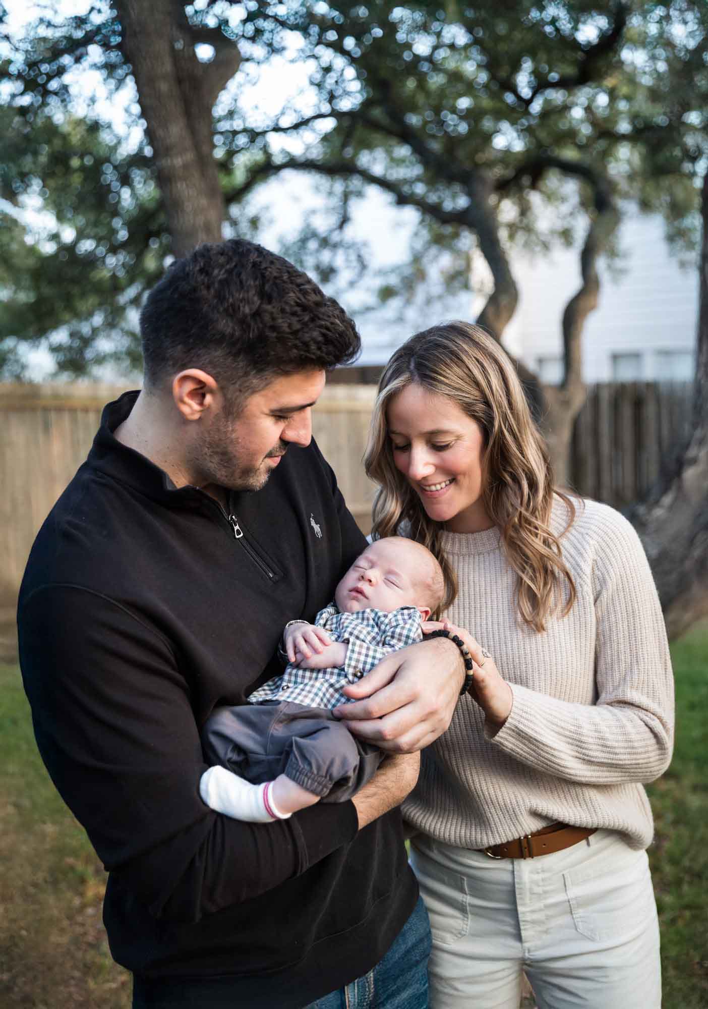 Mother and father looking down at newborn baby boy in backyard during an Austin newborn portrait session