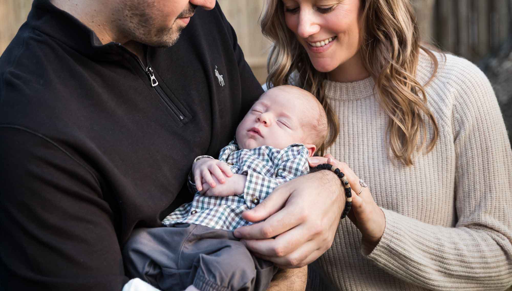 Mother and father looking down at newborn baby boy in backyard during an Austin newborn portrait session