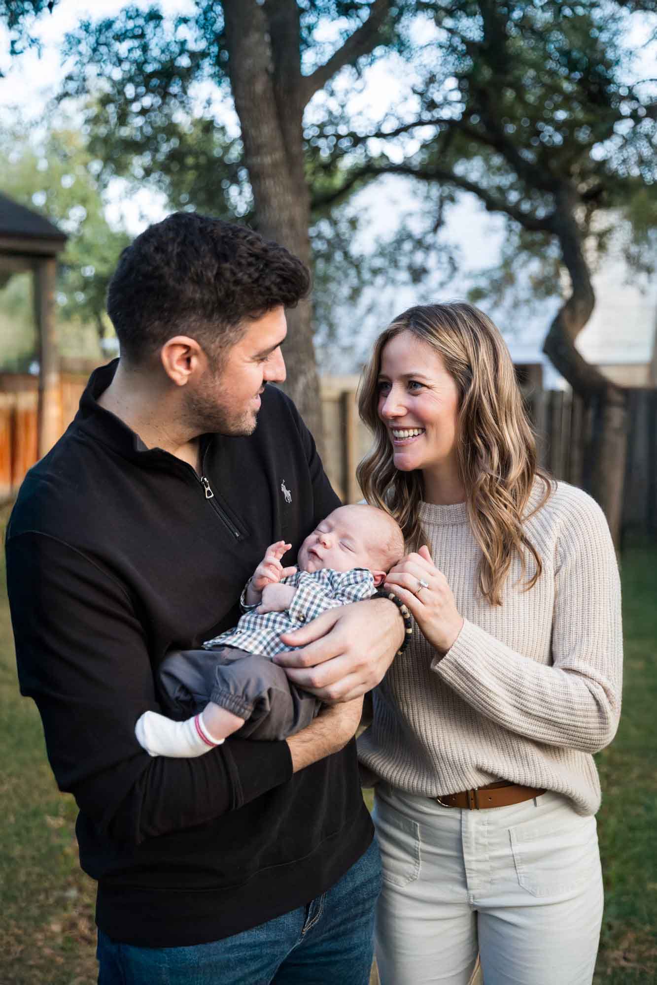 Mother and father looking at each other while holding newborn baby boy in backyard during an Austin newborn portrait session