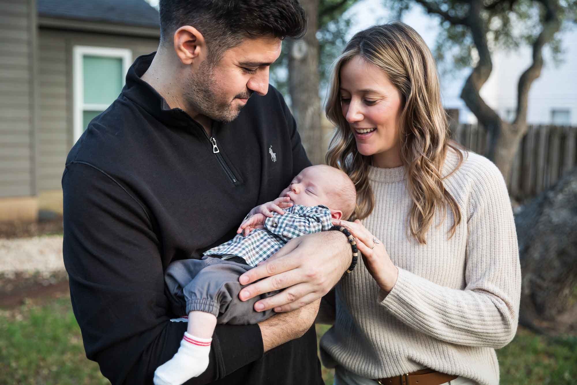 Mother and father looking down at newborn baby boy in backyard during an Austin newborn portrait session