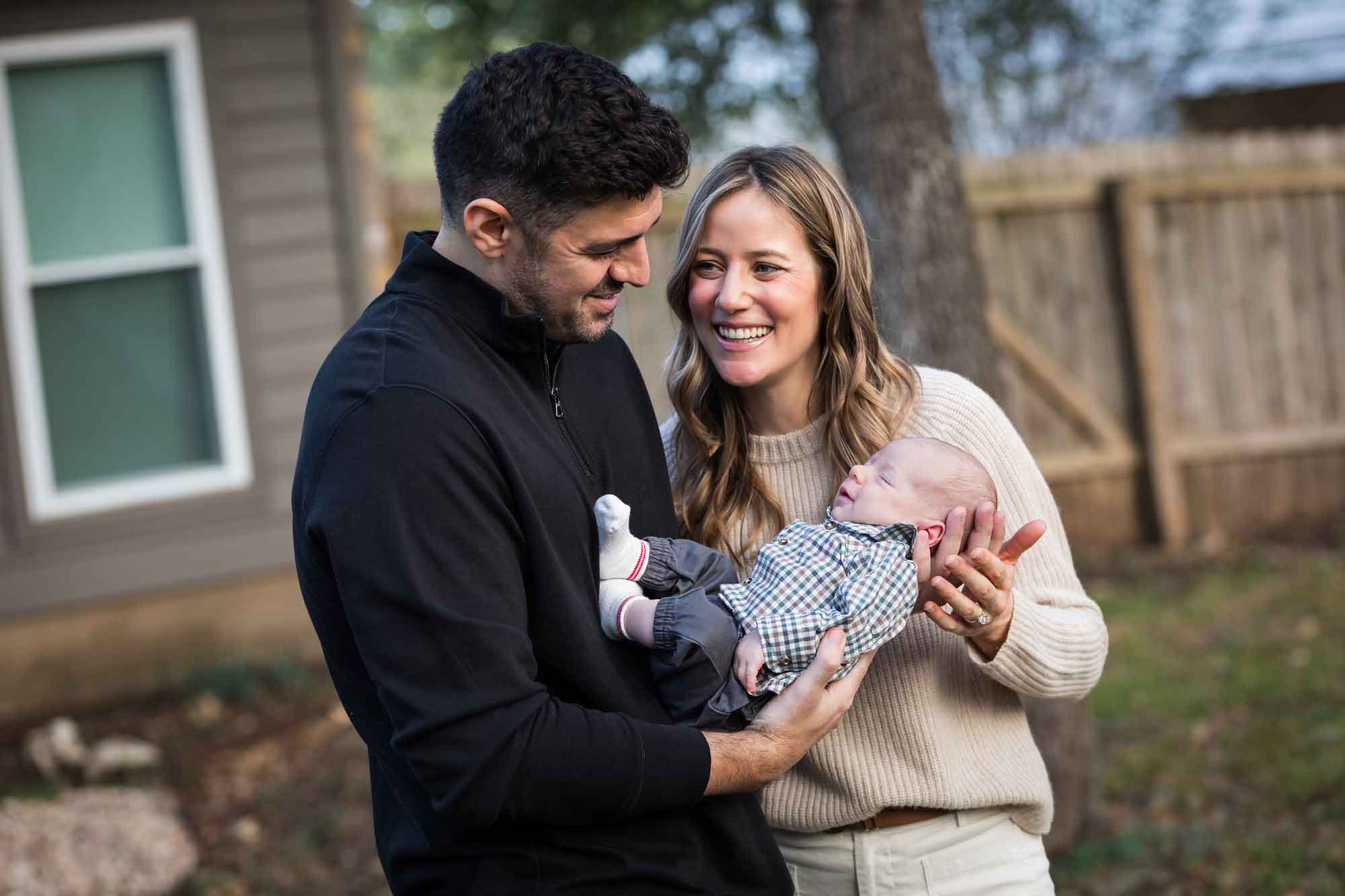 Mother and father looking at each other while holding newborn baby boy in backyard during an Austin newborn portrait session