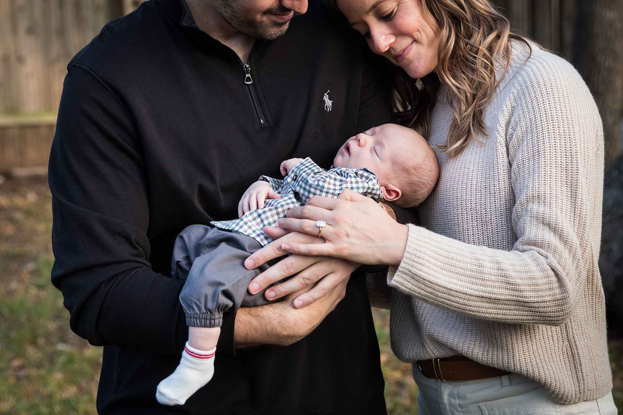 Mother and father looking down at newborn baby boy in backyard during an Austin newborn portrait session