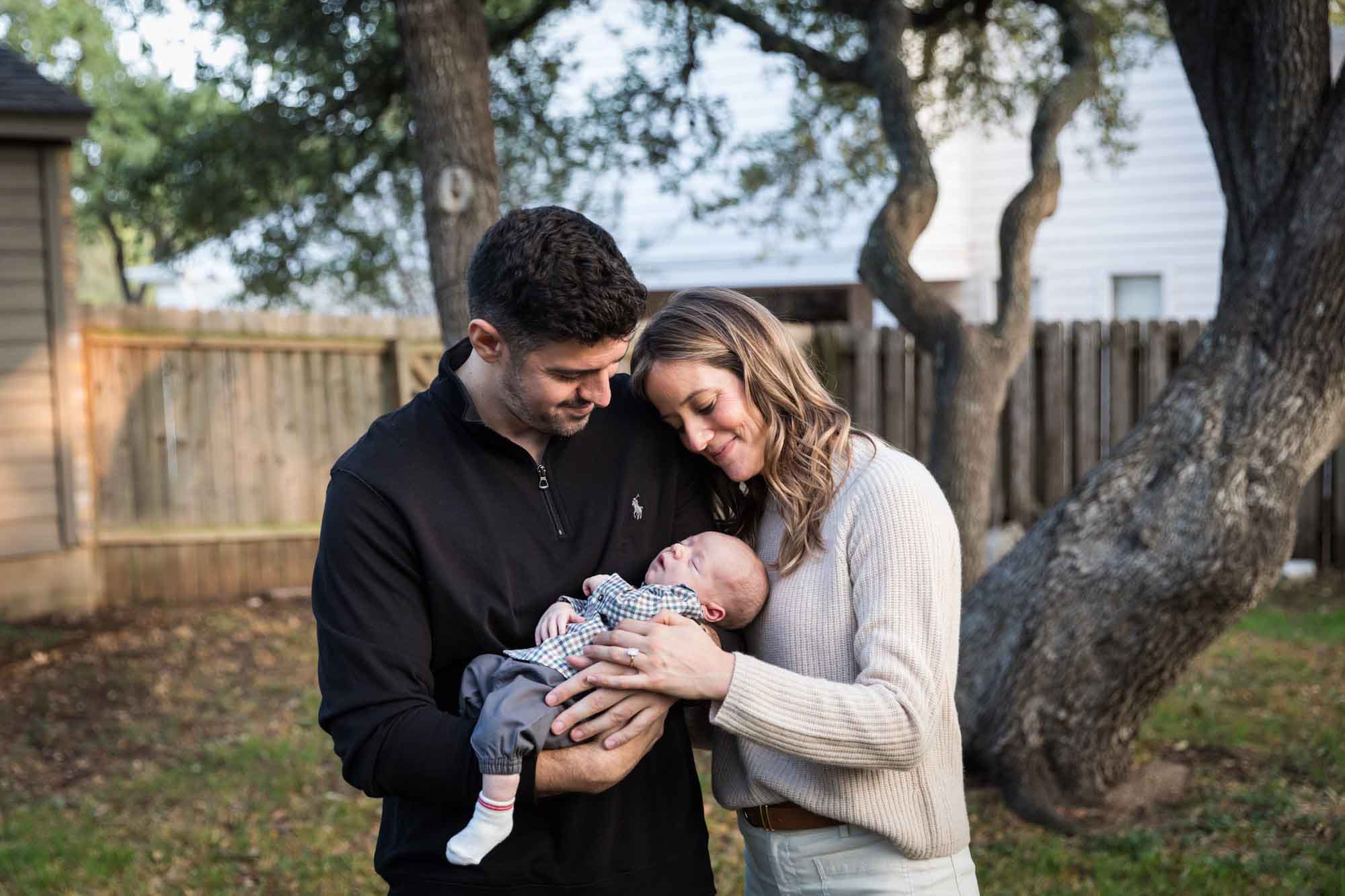 Mother and father looking down at newborn baby boy in backyard during an Austin newborn portrait session