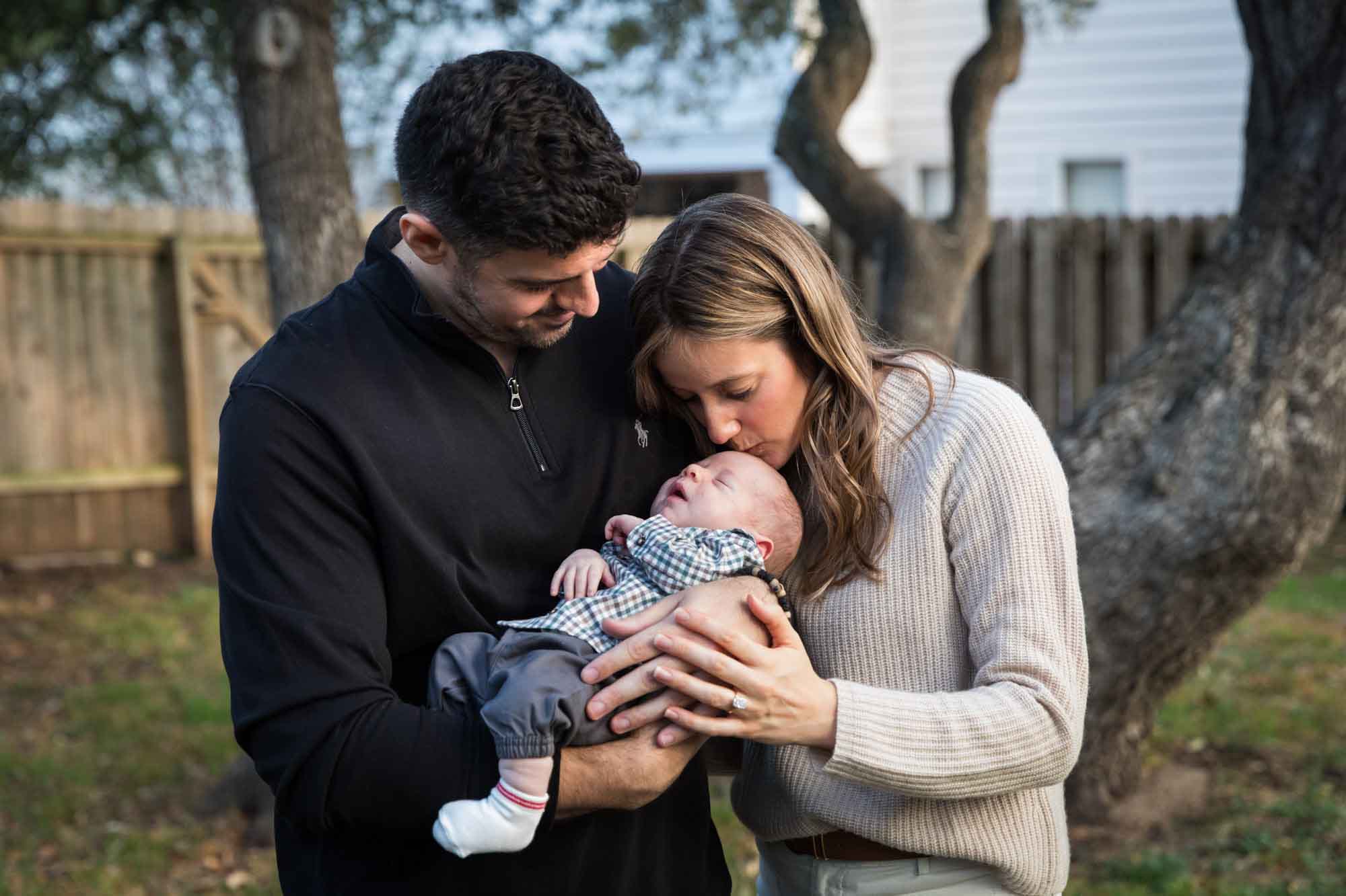 Mother and father looking down at newborn baby boy in backyard during an Austin newborn portrait session