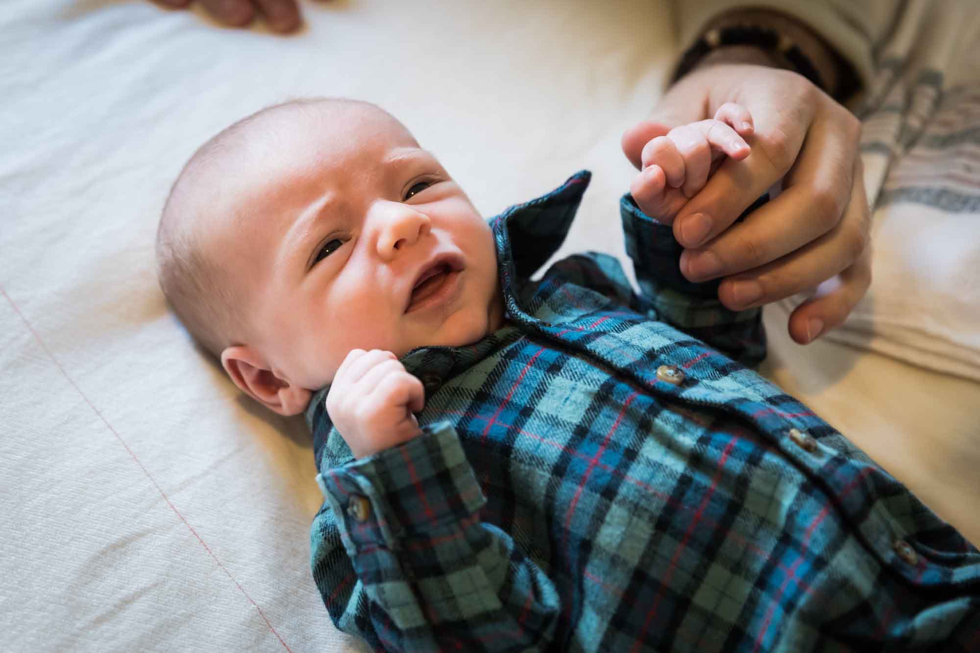 Father's hand holding hand of newborn baby boy wearing blue and green plaid shirt during an Austin newborn portrait session