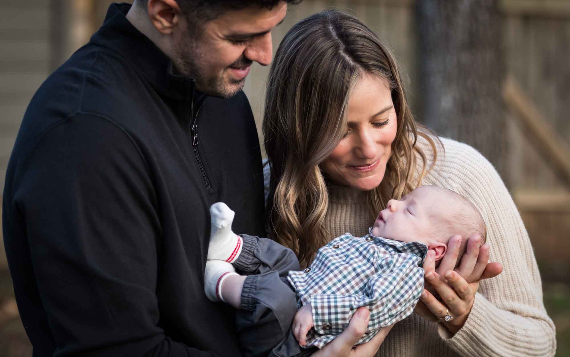 Mother and father looking down at newborn baby boy in backyard during an Austin newborn portrait session