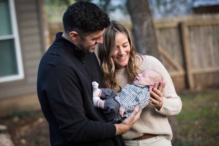 Mother and father looking down at newborn baby boy in backyard during an Austin newborn portrait session