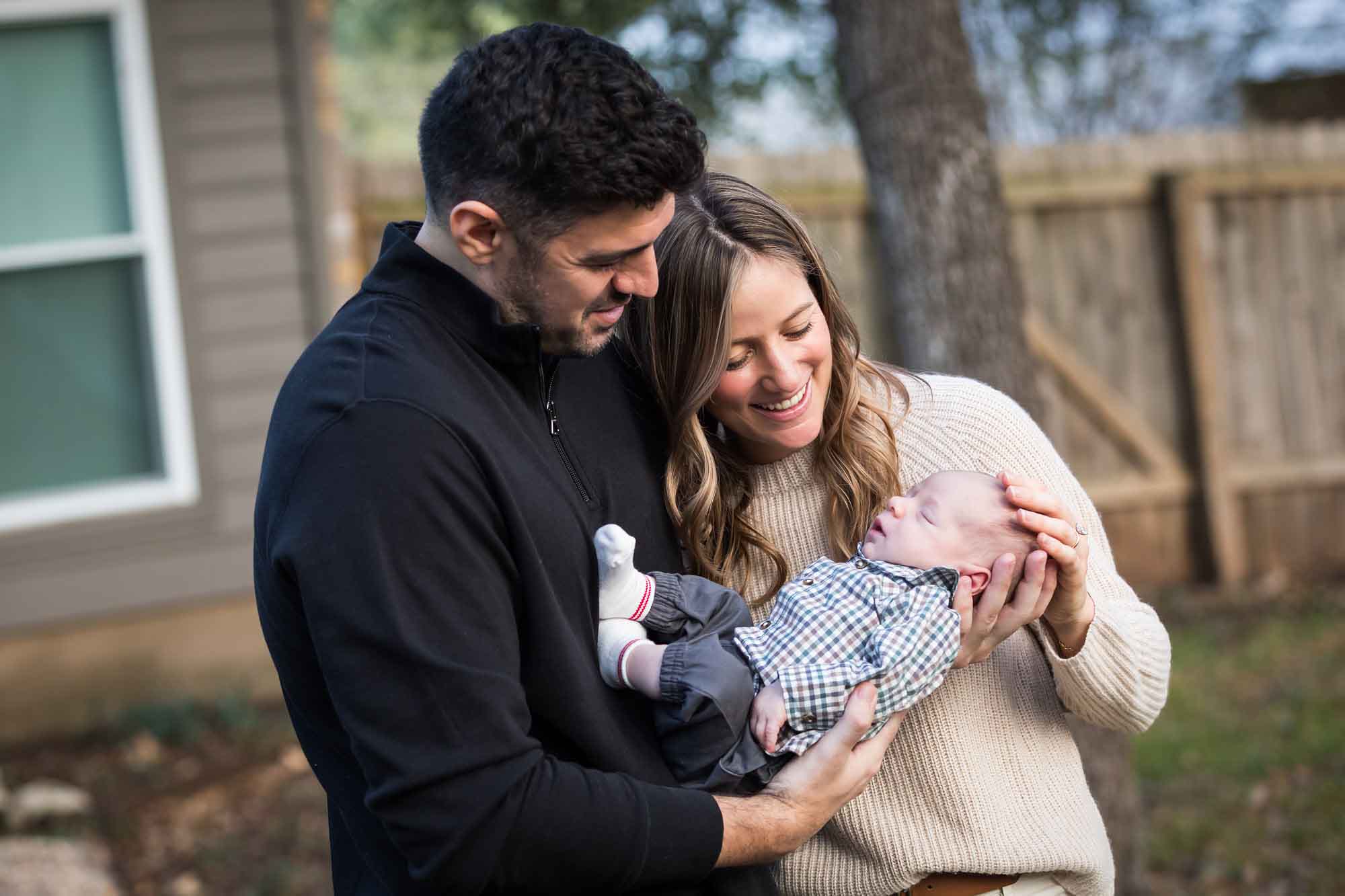 Mother and father looking down at newborn baby boy in backyard during an Austin newborn portrait session