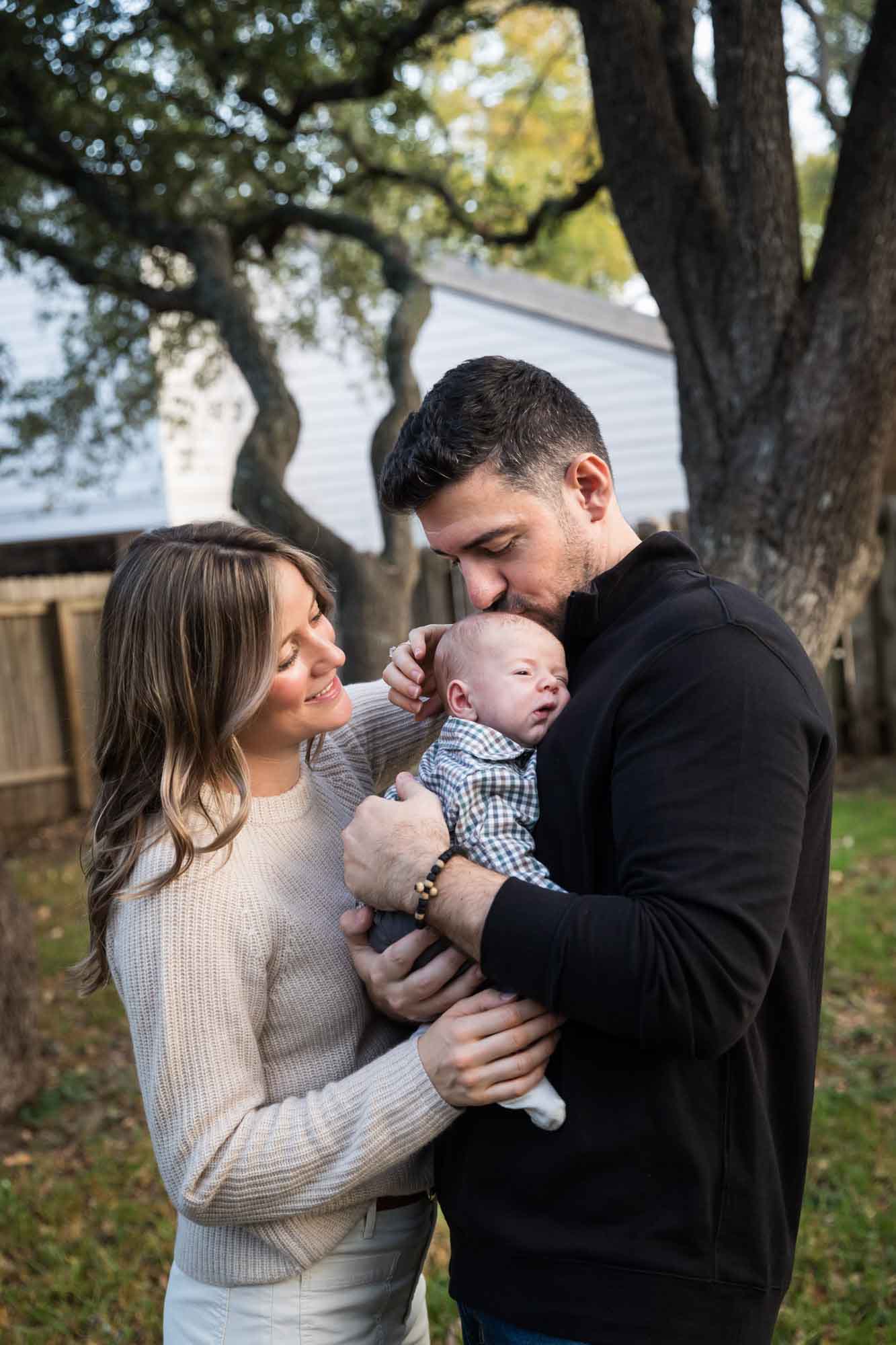 Mother and father looking down at newborn baby boy in backyard during an Austin newborn portrait session